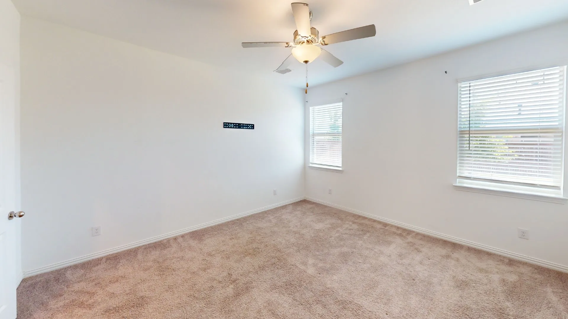Carpeted flooring, ceiling fan, two windows with blinds, and a built-in wall mount