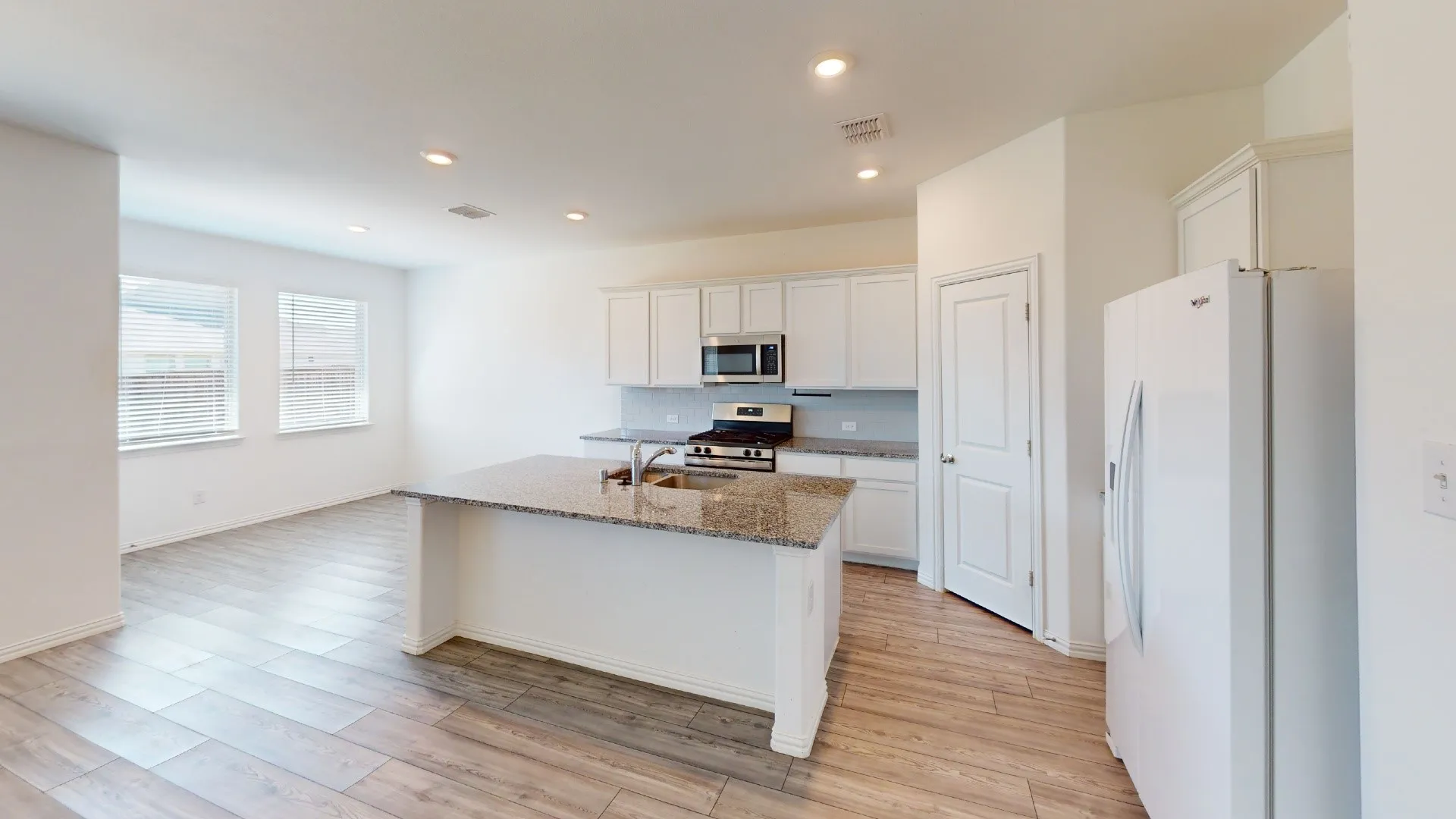 Kitchen island with stone countertop, stainless steel appliances, recessed lighting, wood-finish flooring, and white cabinetry