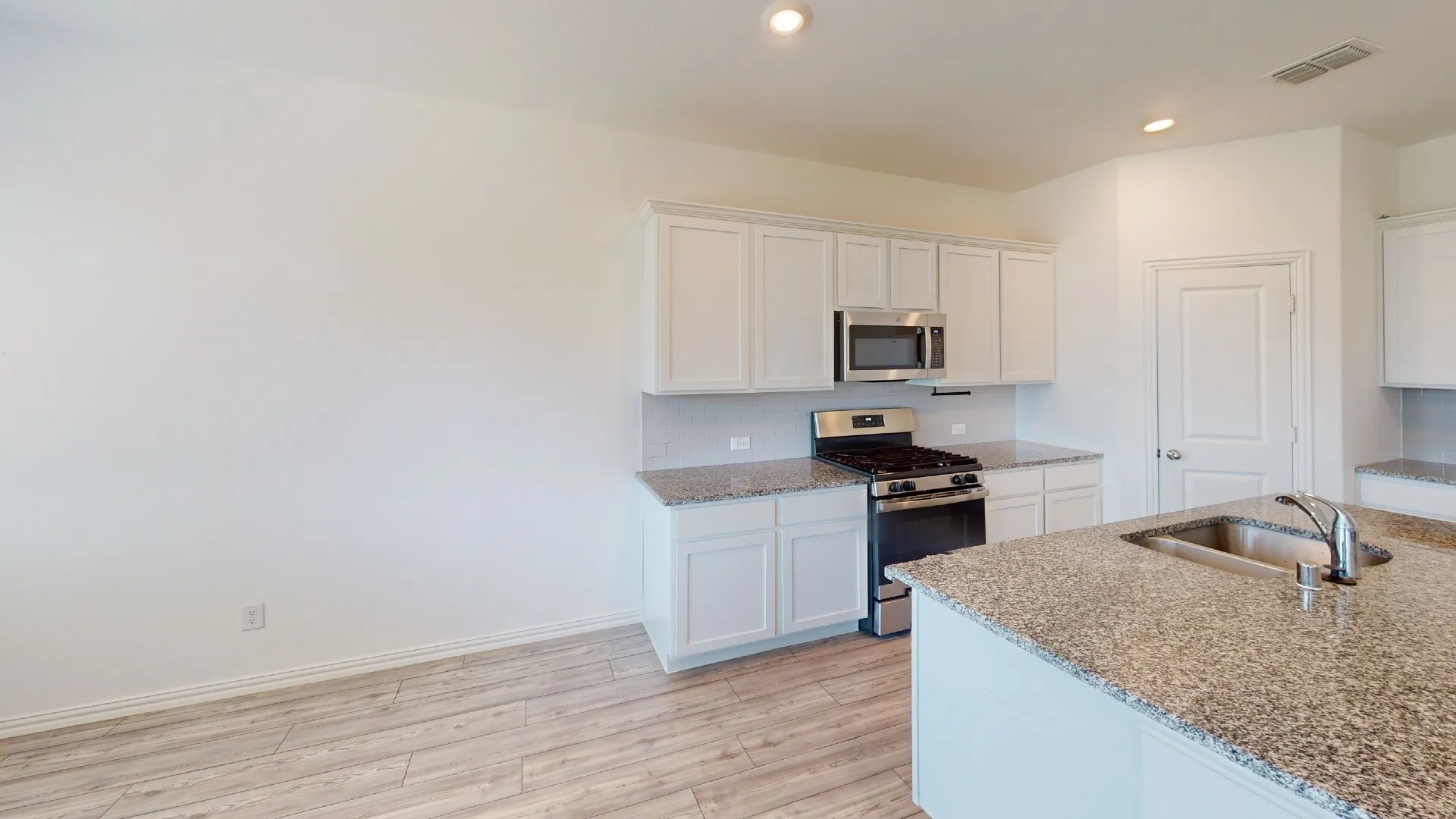 Modern kitchen featuring white cabinetry, stainless steel appliances, wood-finish flooring, and a spacious granite-topped island with seating