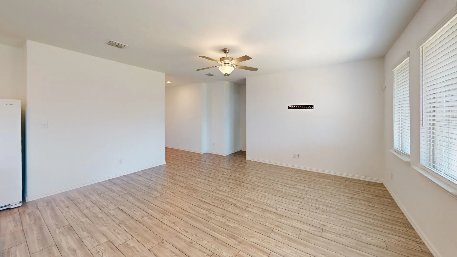 Expansive room with wood-finish flooring, multiple windows with blinds, and a ceiling fan