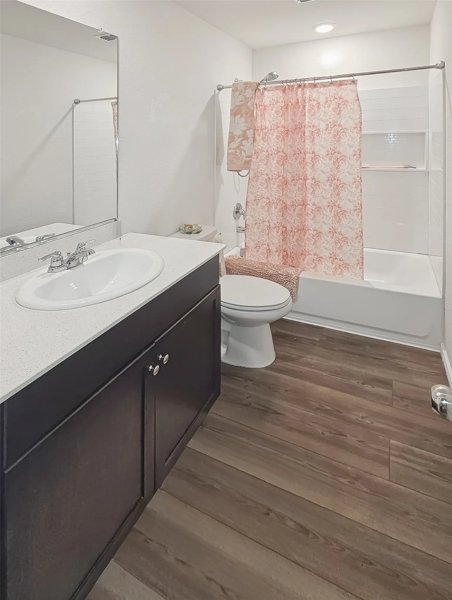 Dark wood-finish flooring, built-in vanity with white countertop, integrated sink, and chrome fixtures