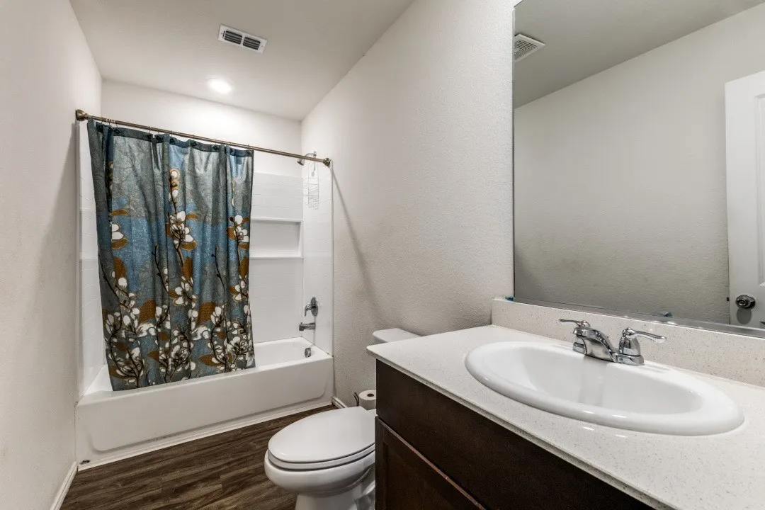 Bathroom featuring a built-in tub with shower, wood-finish flooring, a vanity with an integrated sink, and a wall-mounted mirror