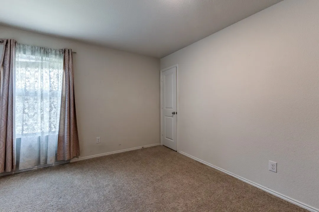 Carpeted flooring, neutral wall tones, window with drapes, and a paneled door