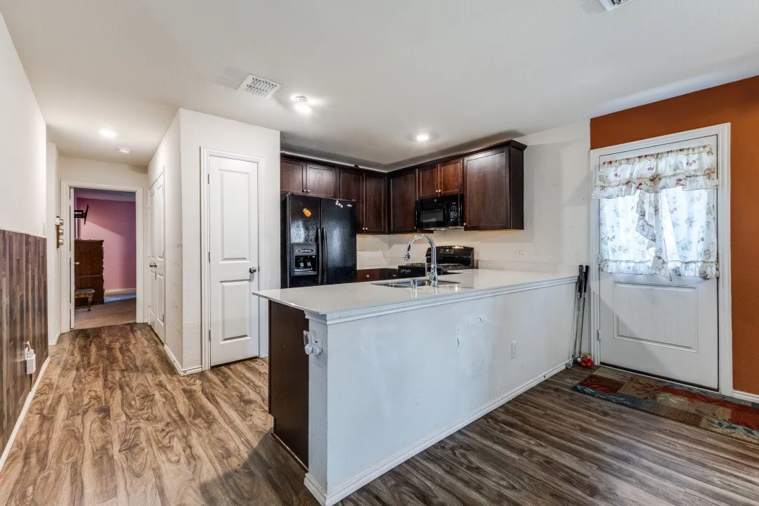 Kitchen featuring dark wood-finish cabinetry, white countertops, a black refrigerator, and an integrated kitchen island with a sink