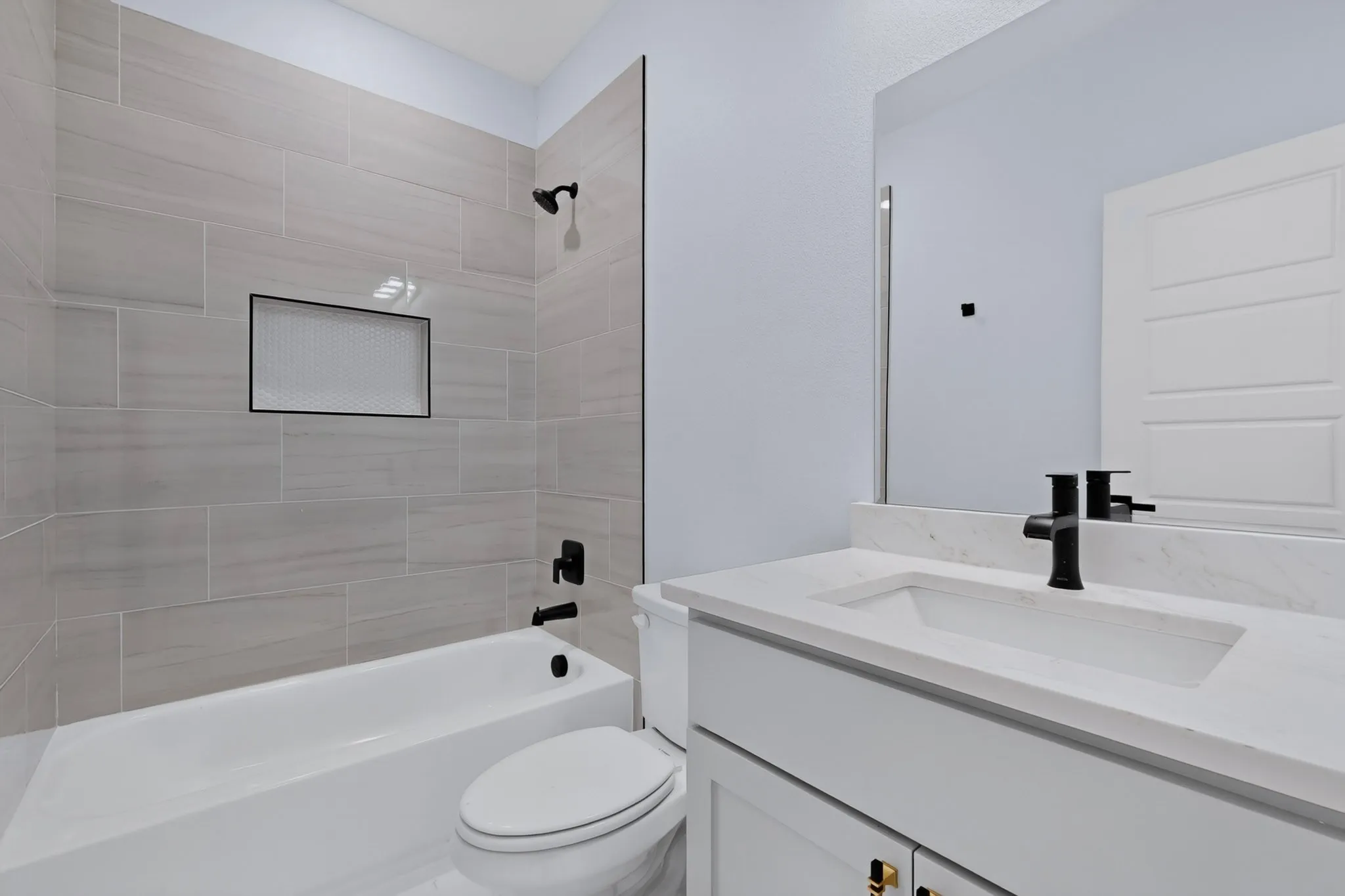 Bathtub with light-toned tiled surround, integrated shower niche, and matte black fixtures