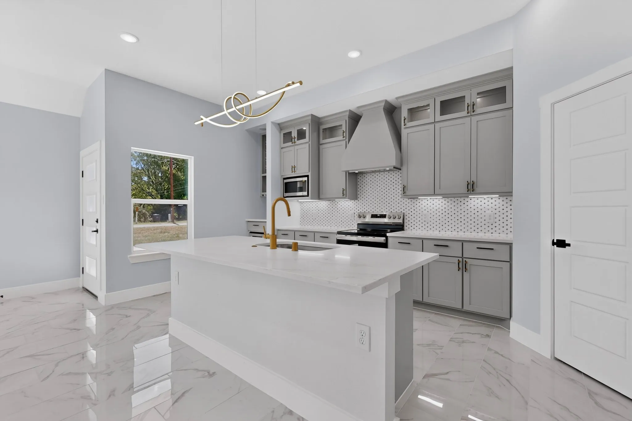 Kitchen featuring a central island with a countertop, gray cabinetry, stainless steel appliances, a honeycomb tile backsplash, and a modern light fixture