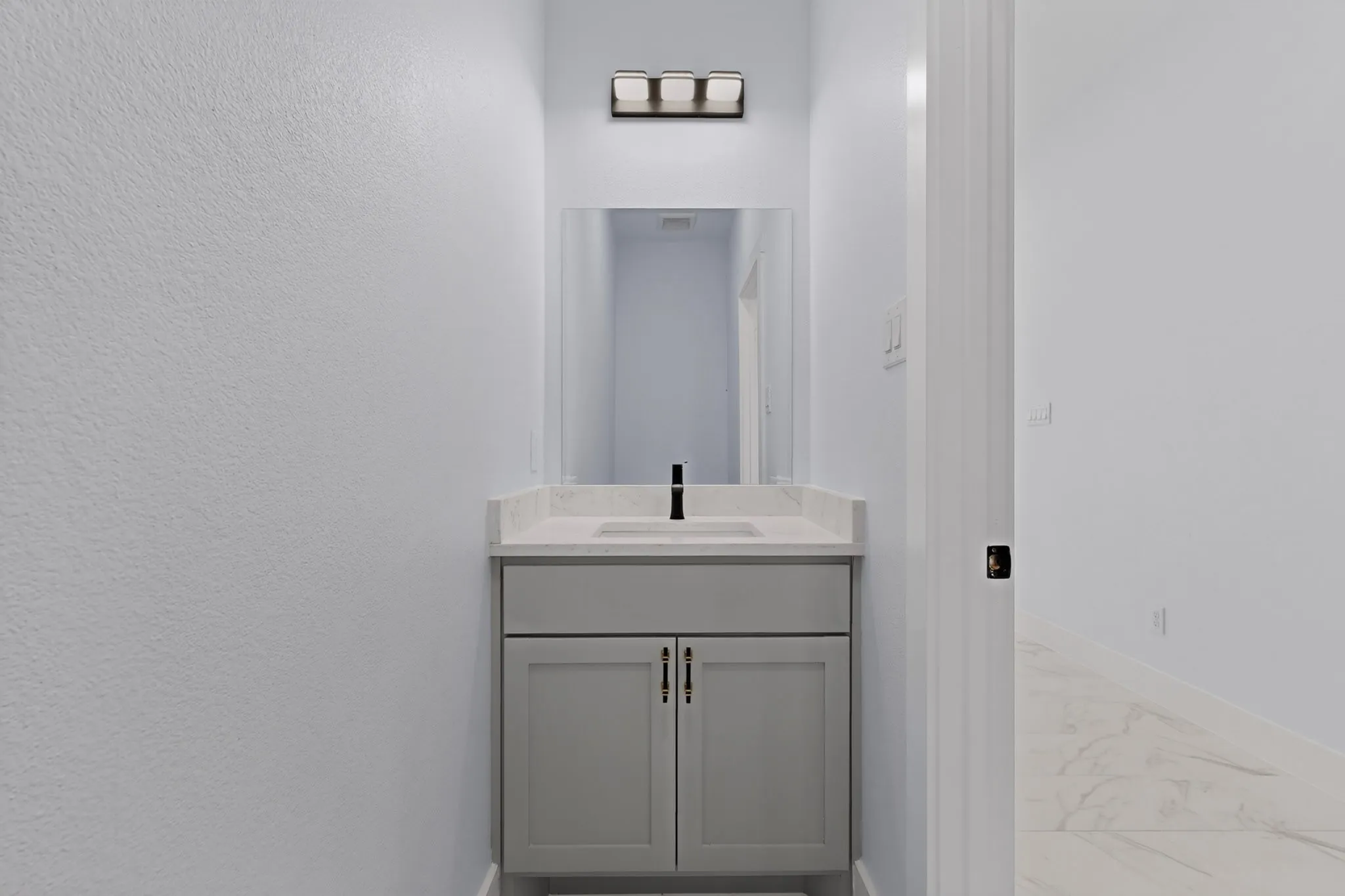 Powder room featuring a single vanity with gray cabinetry, a rectangular undermount sink, and a light-toned countertop