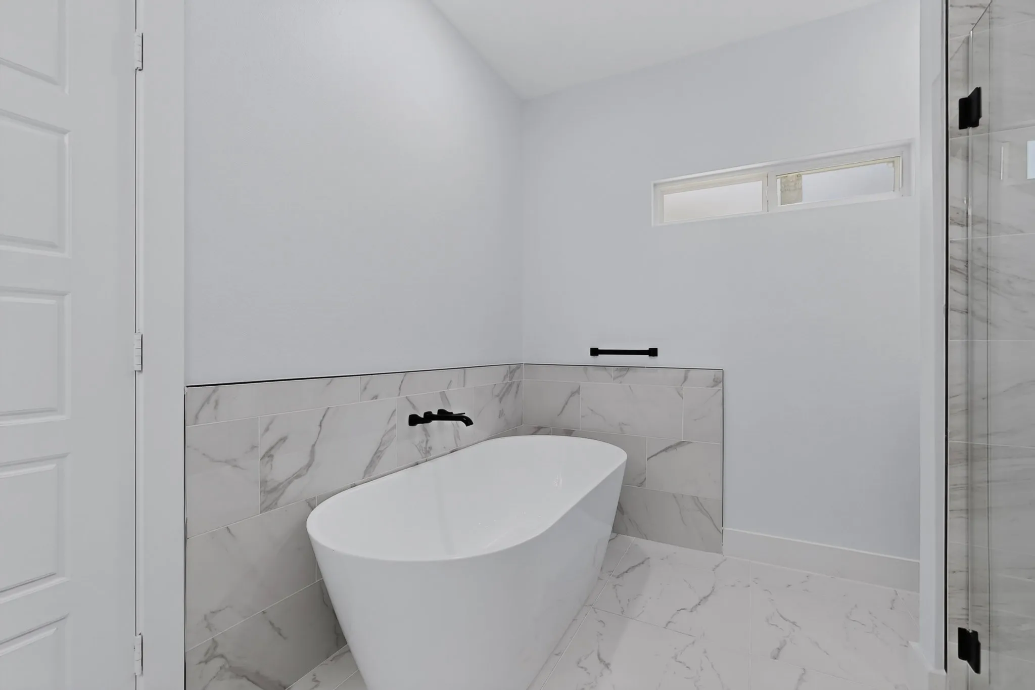 Freestanding soaking tub with matte black fixtures, marble-look tile surround, and a clear glass shower enclosure