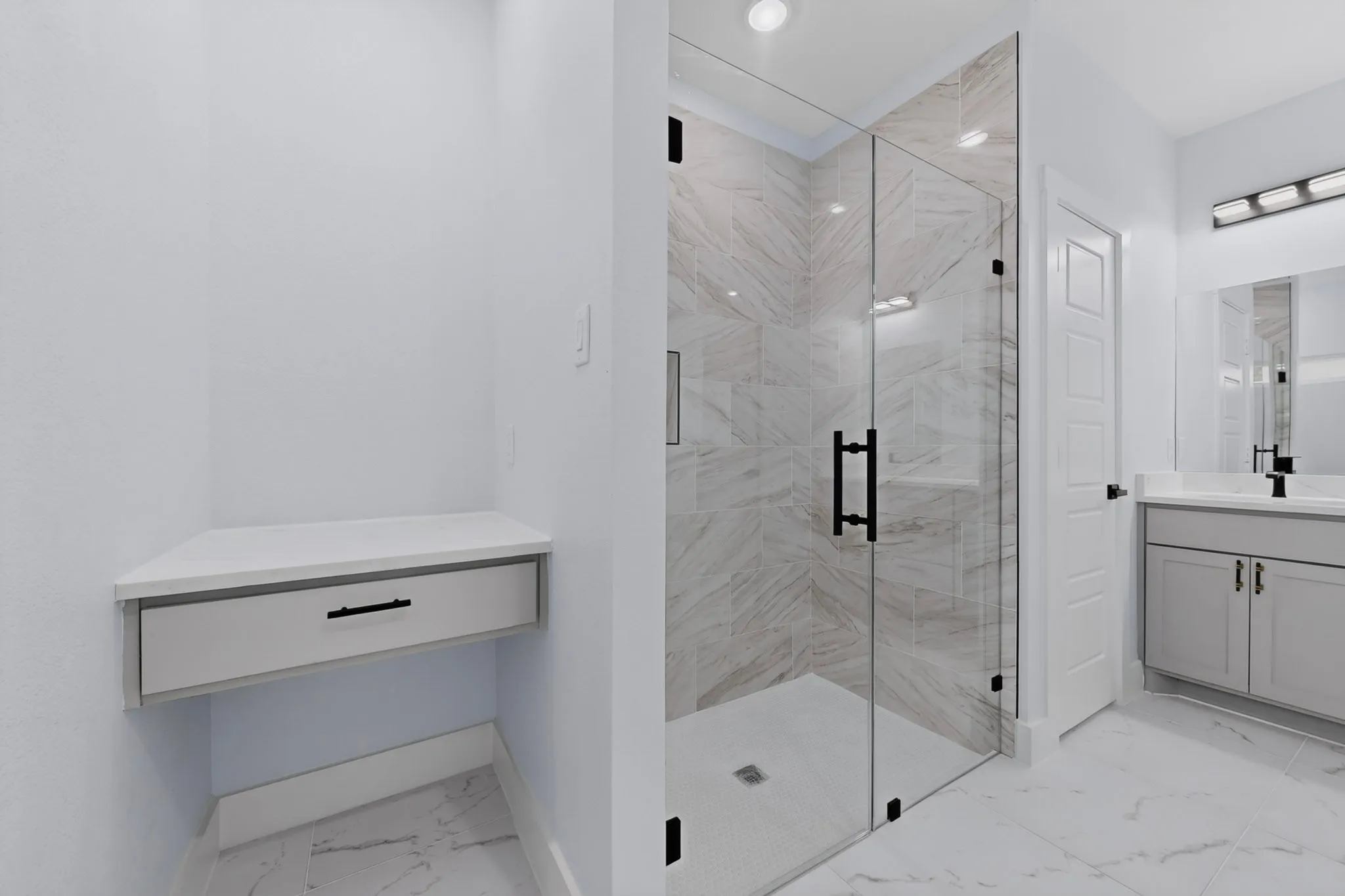 Corner vanity with drawer, glass-enclosed shower with tile surround, single vanity with under-sink storage, and large format floor tiling