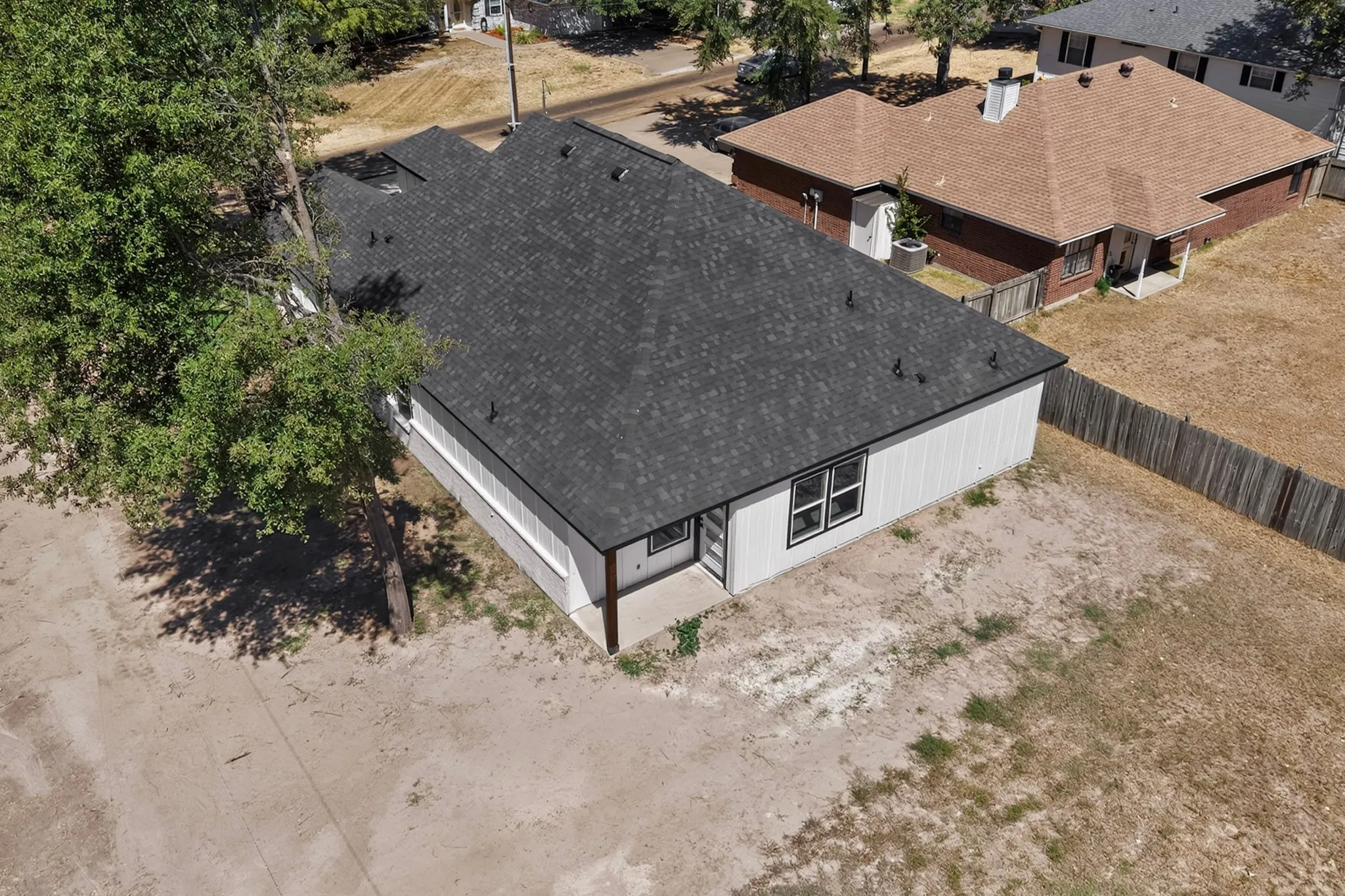 Newly constructed residence featuring a dark shingle roof, white vertical siding, and a rear patio