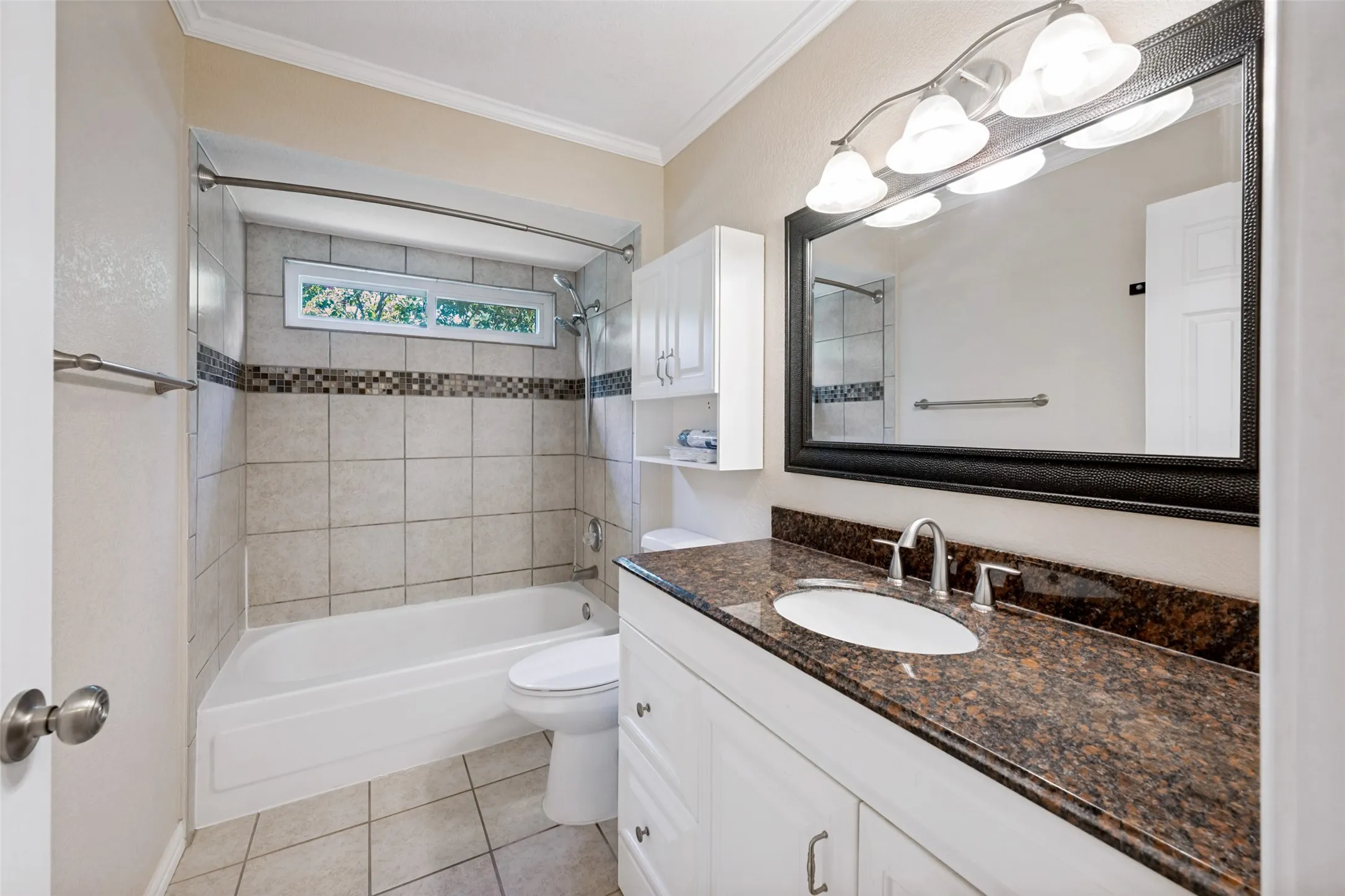 Bathroom featuring a tub/shower combination with tile surround and decorative accent band, a white vanity with a brown speckled countertop, and an integrated rectangular sink with a chrome faucet