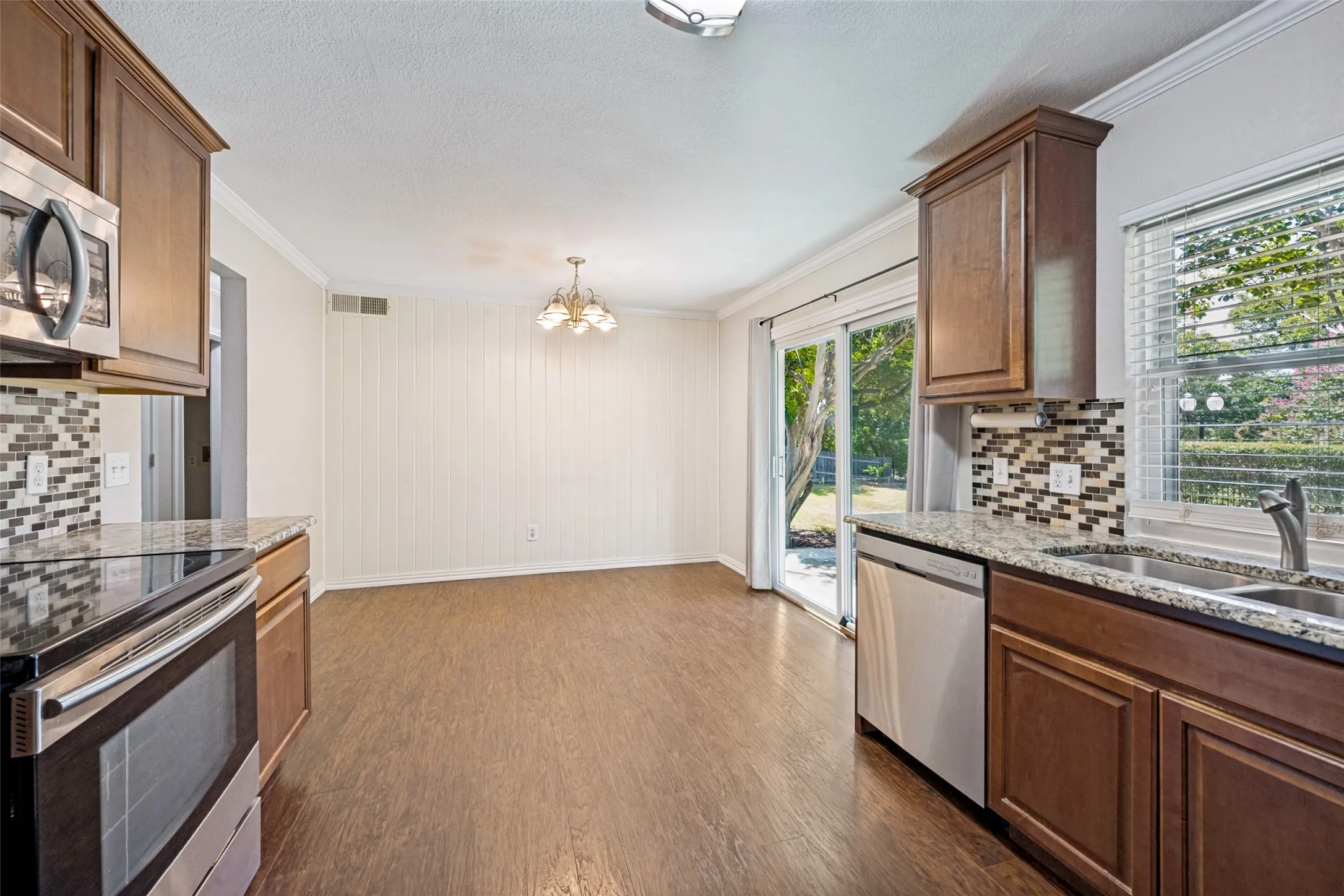 Kitchen featuring wood-finish flooring, stainless steel appliances, granite countertops, and a mosaic tile backsplash