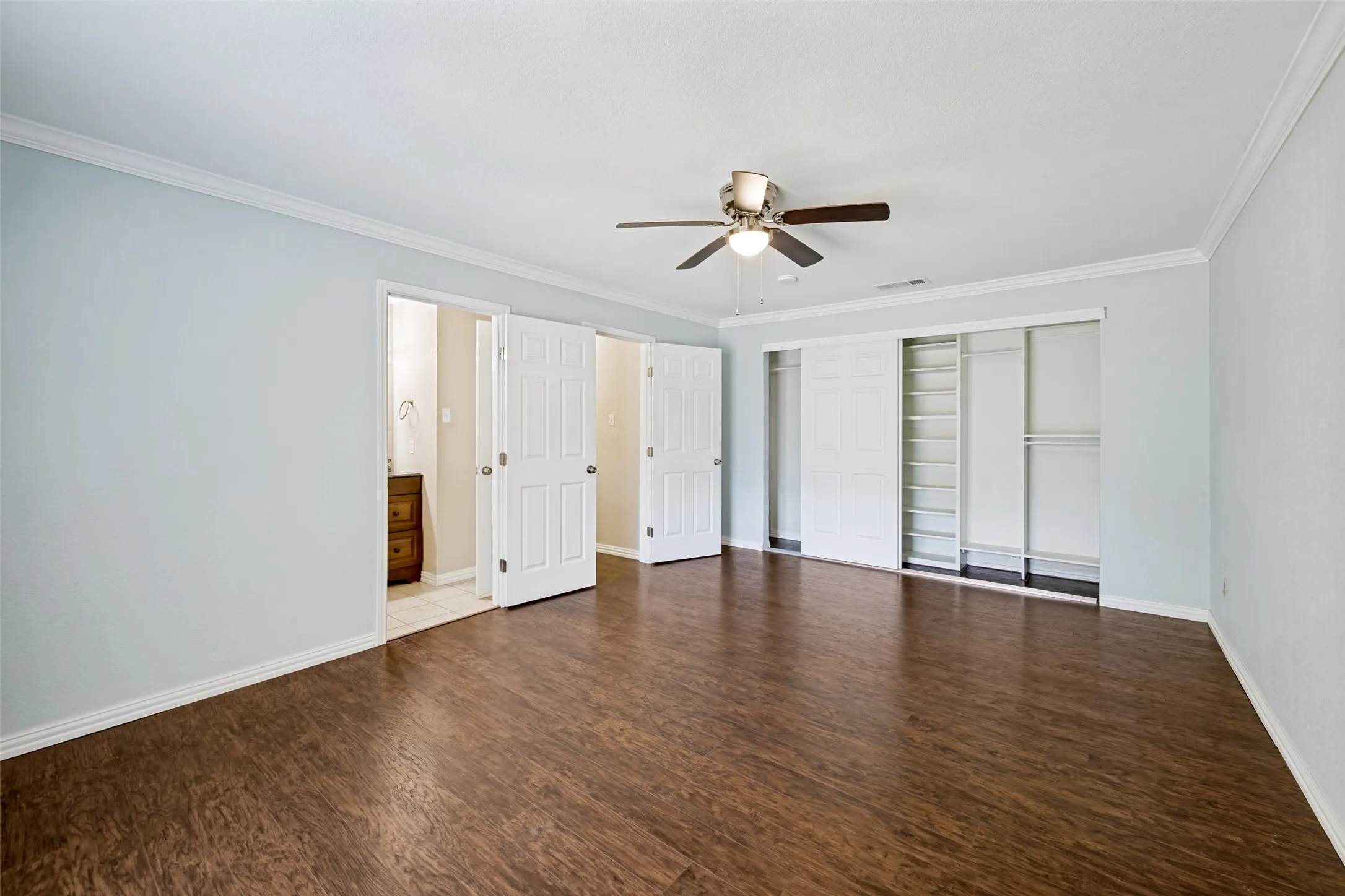 Spacious room featuring wood-finish flooring, a ceiling fan, and sliding closet doors with built-in shelving