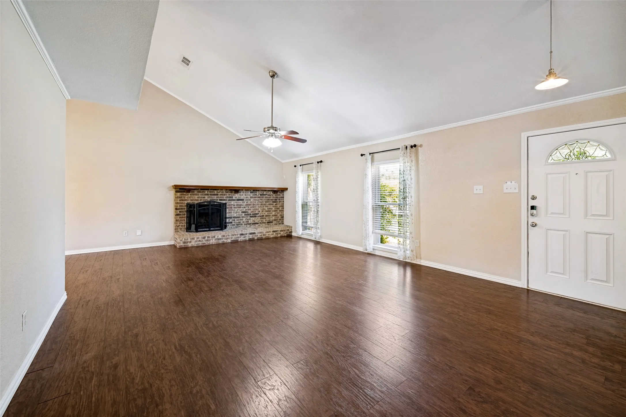 Vaulted ceiling with a ceiling fan, brick fireplace, wood-finish flooring, and a decorative glass front door