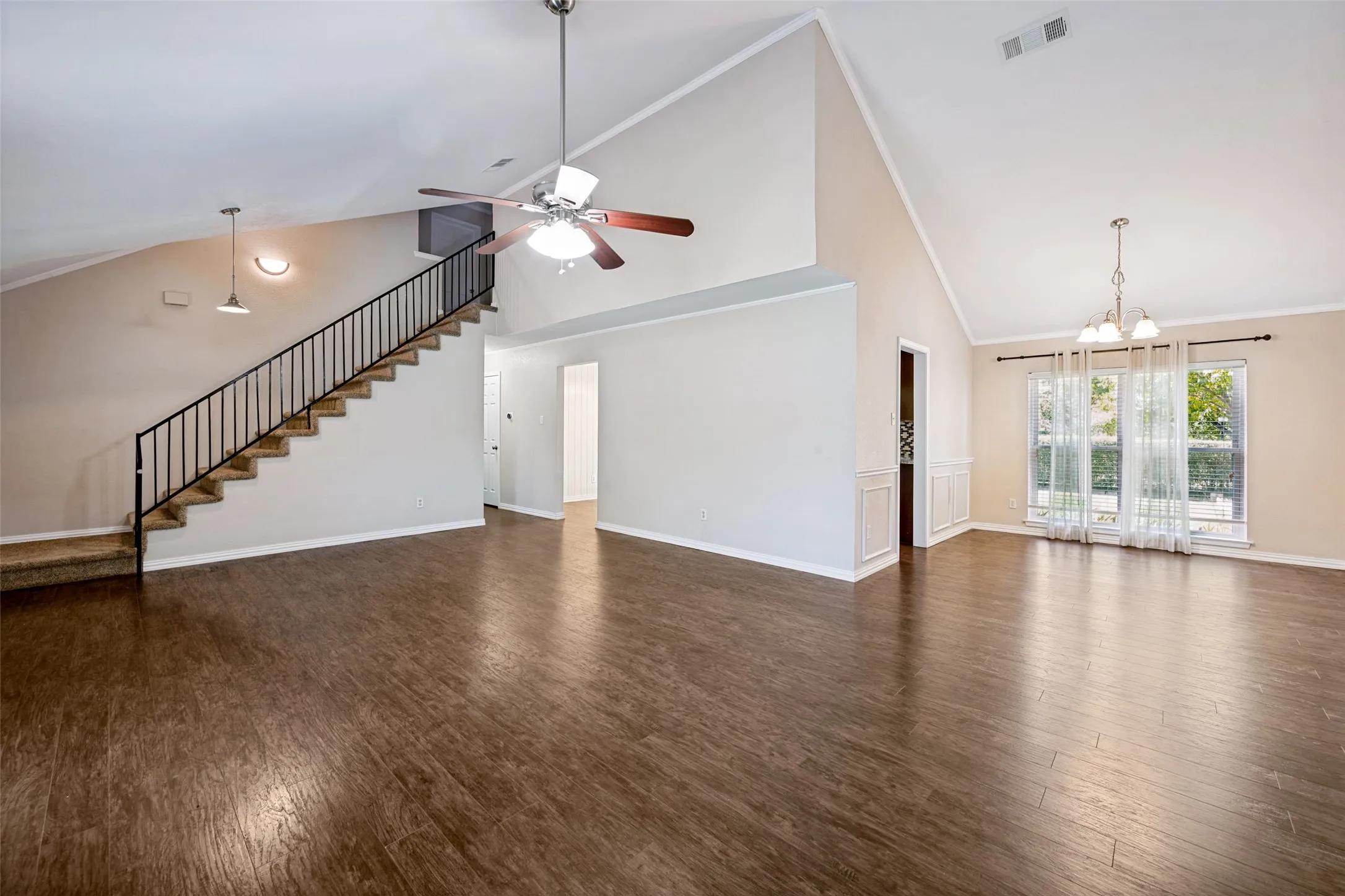 Vaulted ceiling, wood-finish flooring, staircase with metal railing, ceiling fan, and chandelier