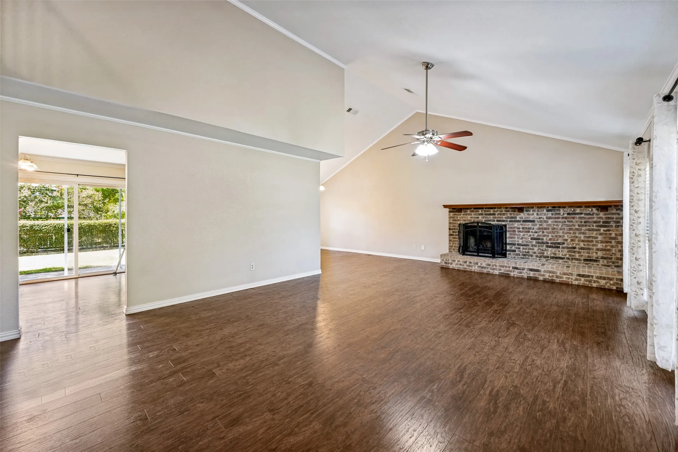 Vaulted ceilings, wood-finish flooring, brick fireplace with mantel, ceiling fan, and sliding glass door