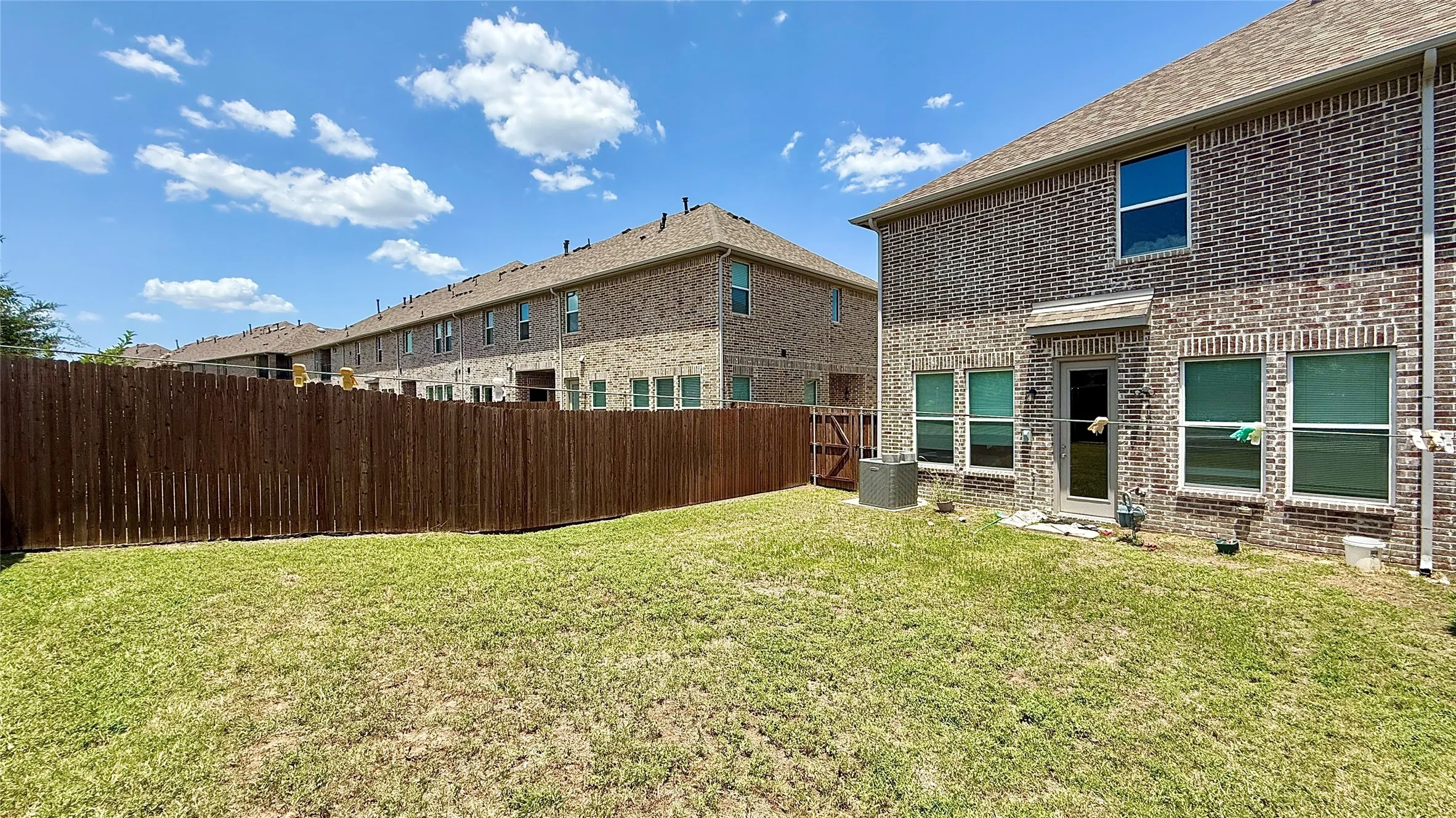 Expansive backyard featuring a manicured lawn, full privacy fence, and brick exterior with multiple windows