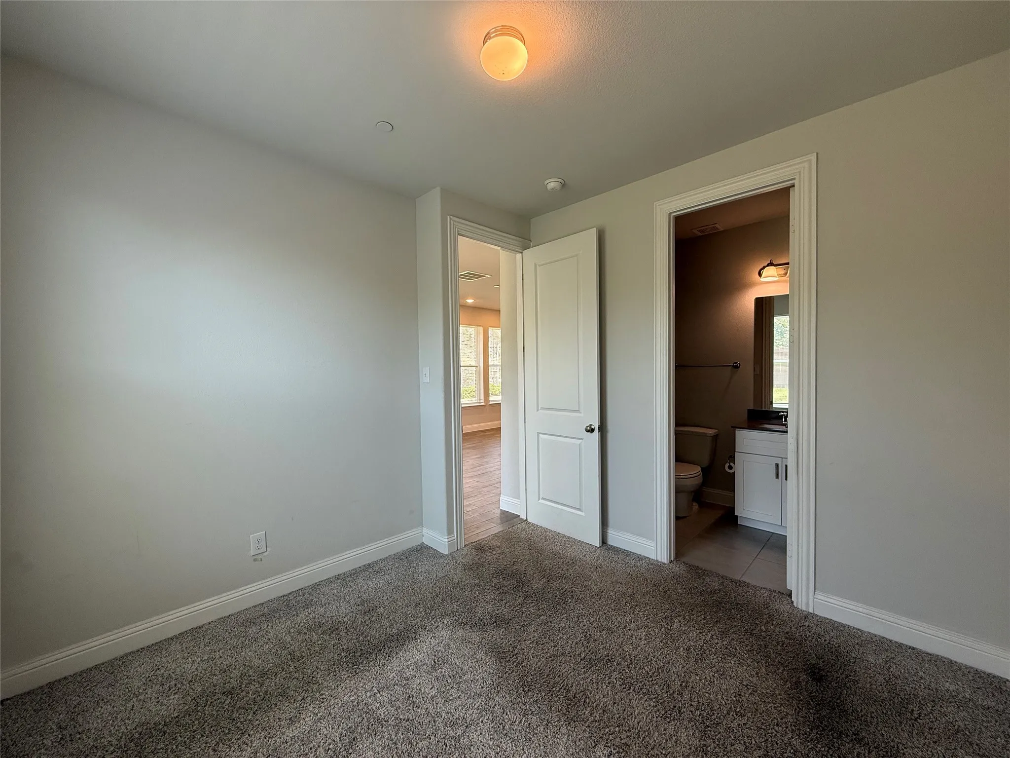 Neutral tone wall paint, textured carpet flooring, white interior doors, and a bathroom with tile flooring and a vanity with a rectangular mirror