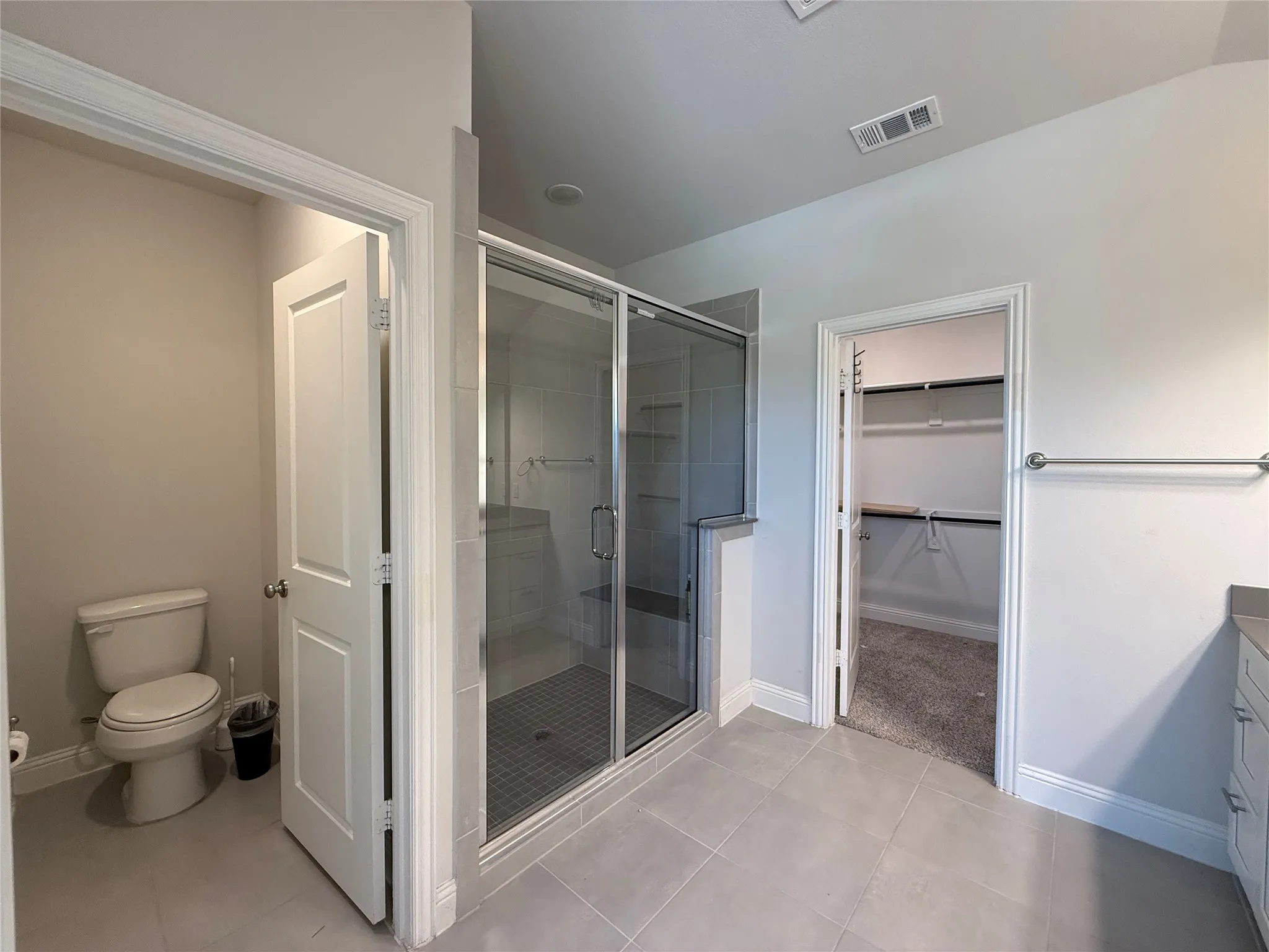 Spacious bathroom featuring a glass-enclosed shower, large format tile flooring, and separate water closet
