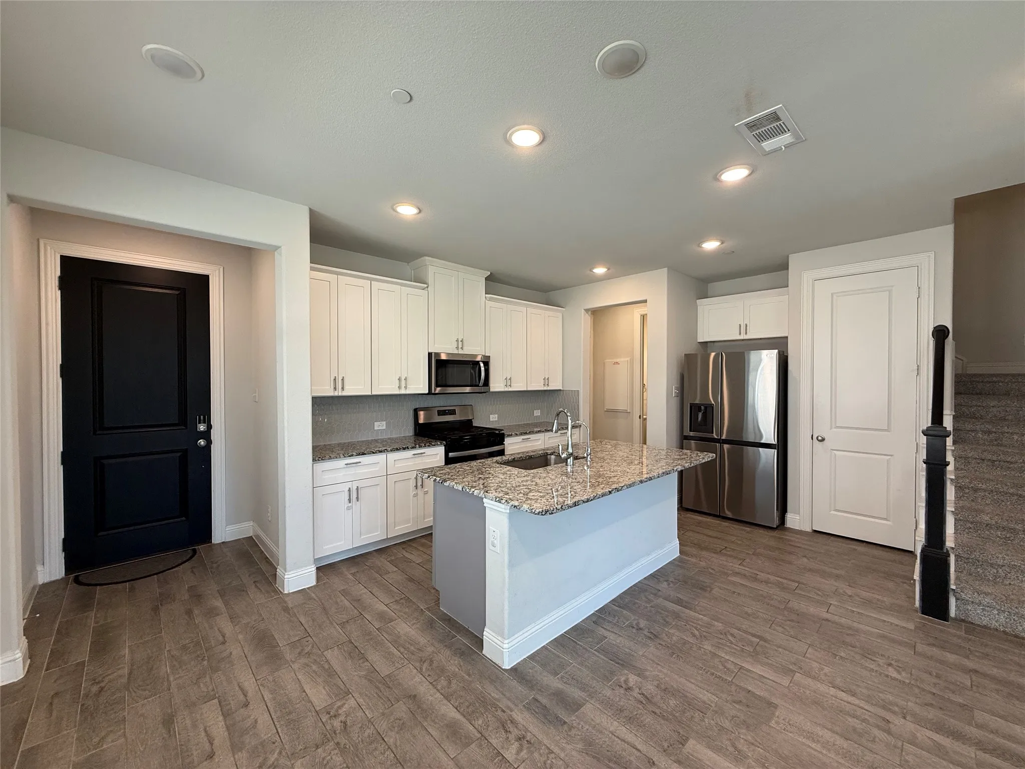 Open concept kitchen featuring white cabinetry, stainless steel appliances, a center island with a sink, and wood-finish flooring
