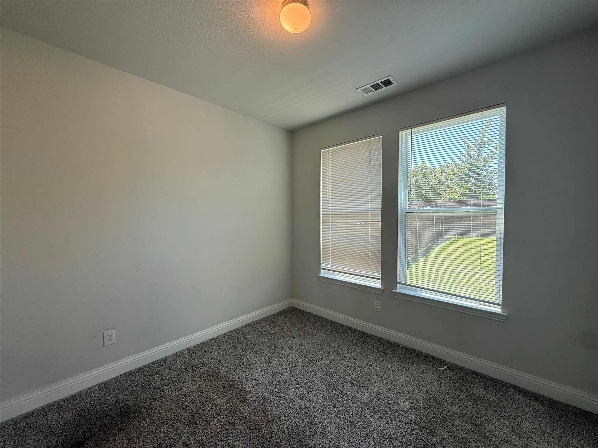 Wall-to-wall carpeting with light-toned walls, two windows with blinds, and an overhead light fixture
