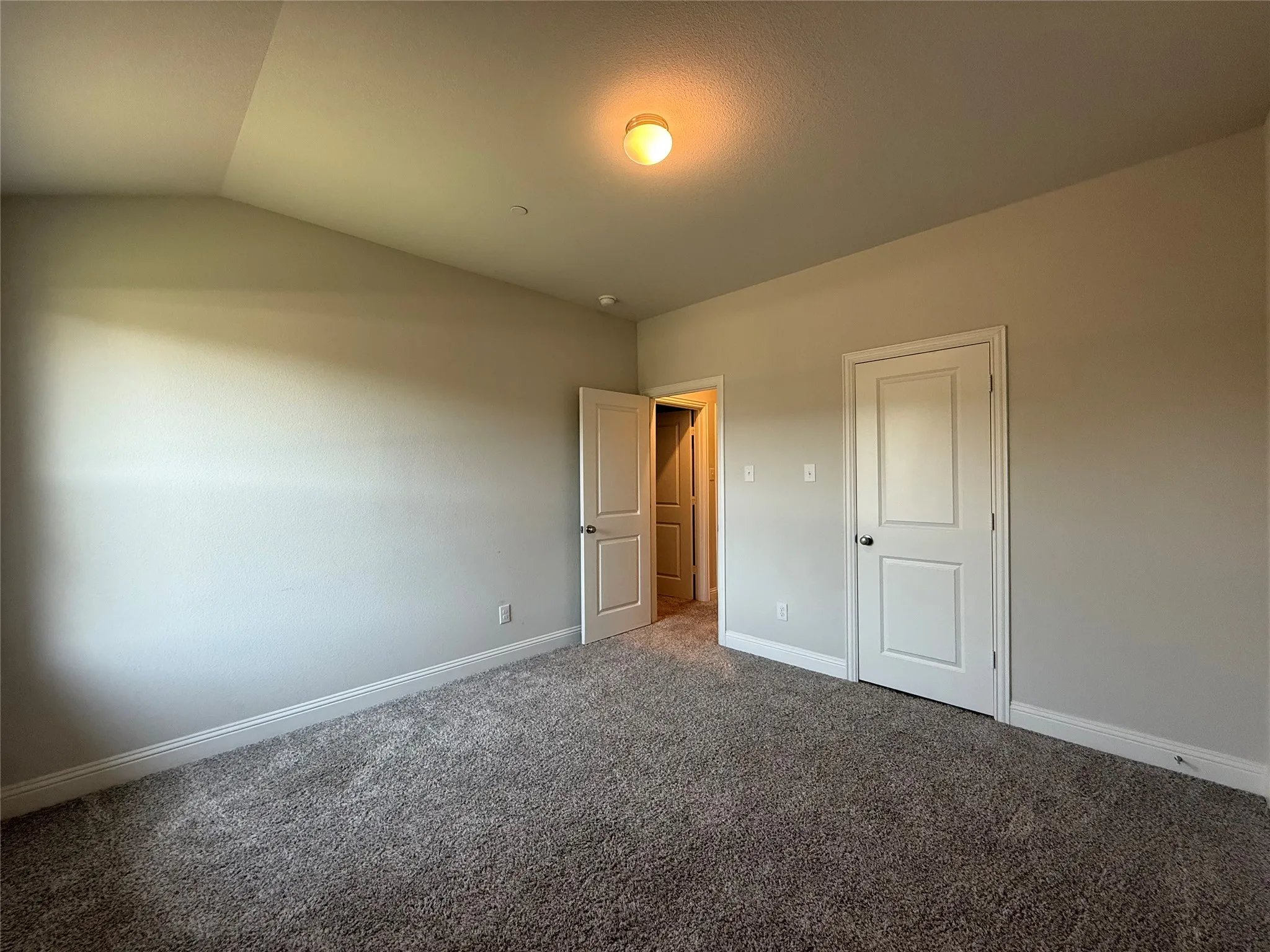 Vaulted ceiling with an attached light fixture, neutral wall paint, and gray carpet flooring