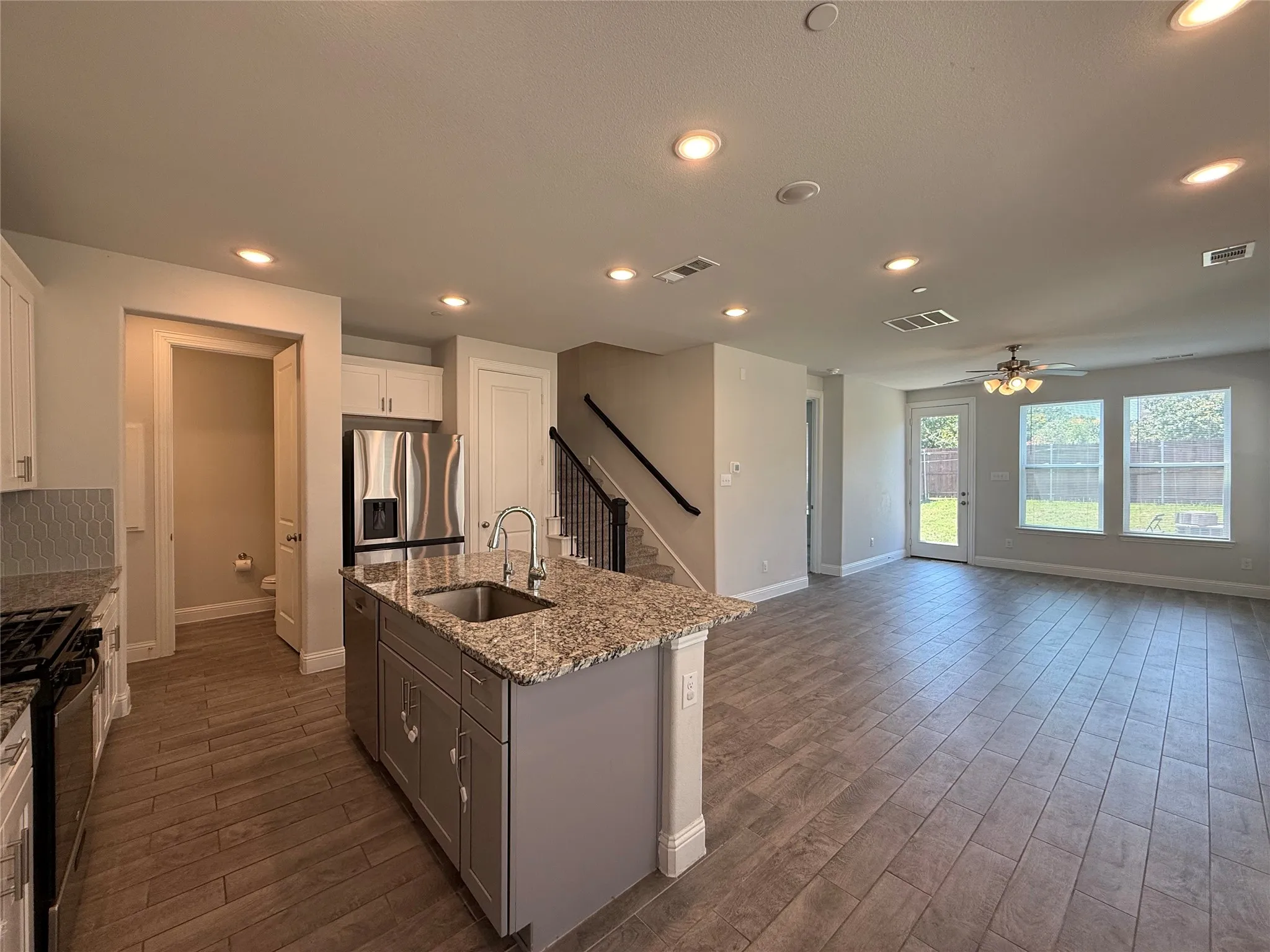 Open-concept living space featuring wood-finish tile flooring, recessed lighting, and a kitchen island with granite countertops