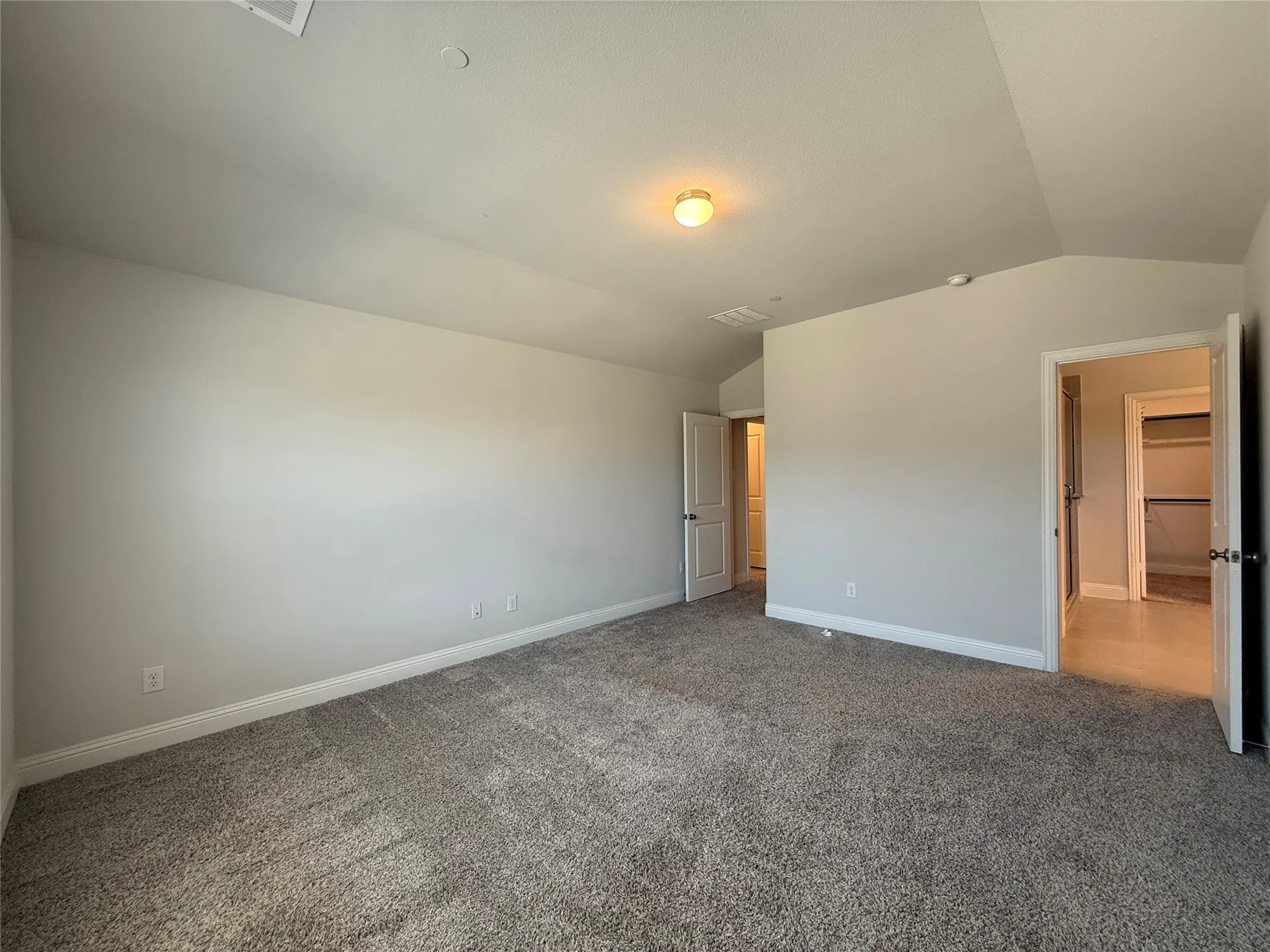 Spacious room featuring vaulted ceilings, neutral-toned walls, and plush carpet flooring