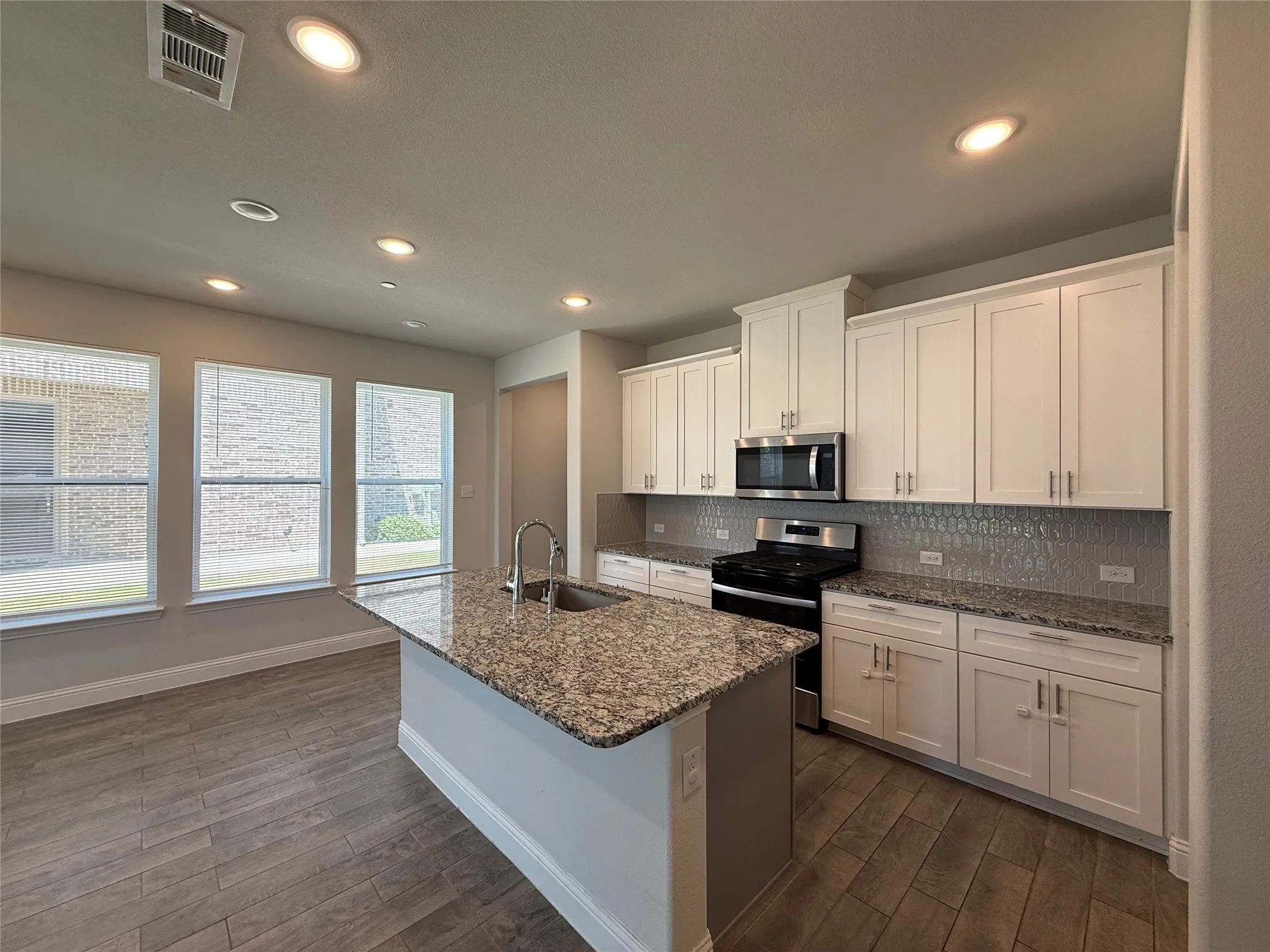 Contemporary kitchen featuring an island with a stainless steel sink, granite countertops, wood-finish flooring, white cabinetry, and stainless steel appliances