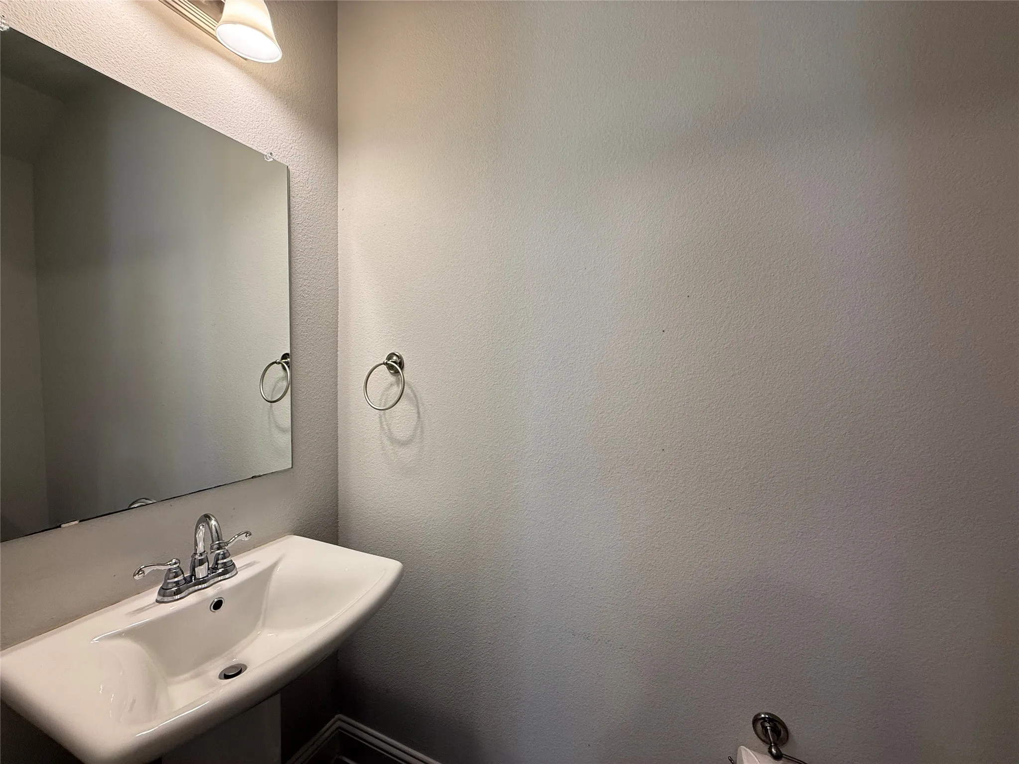 Pedestal sink with chrome-finish faucet, wall-mounted mirror, and overhead vanity lighting