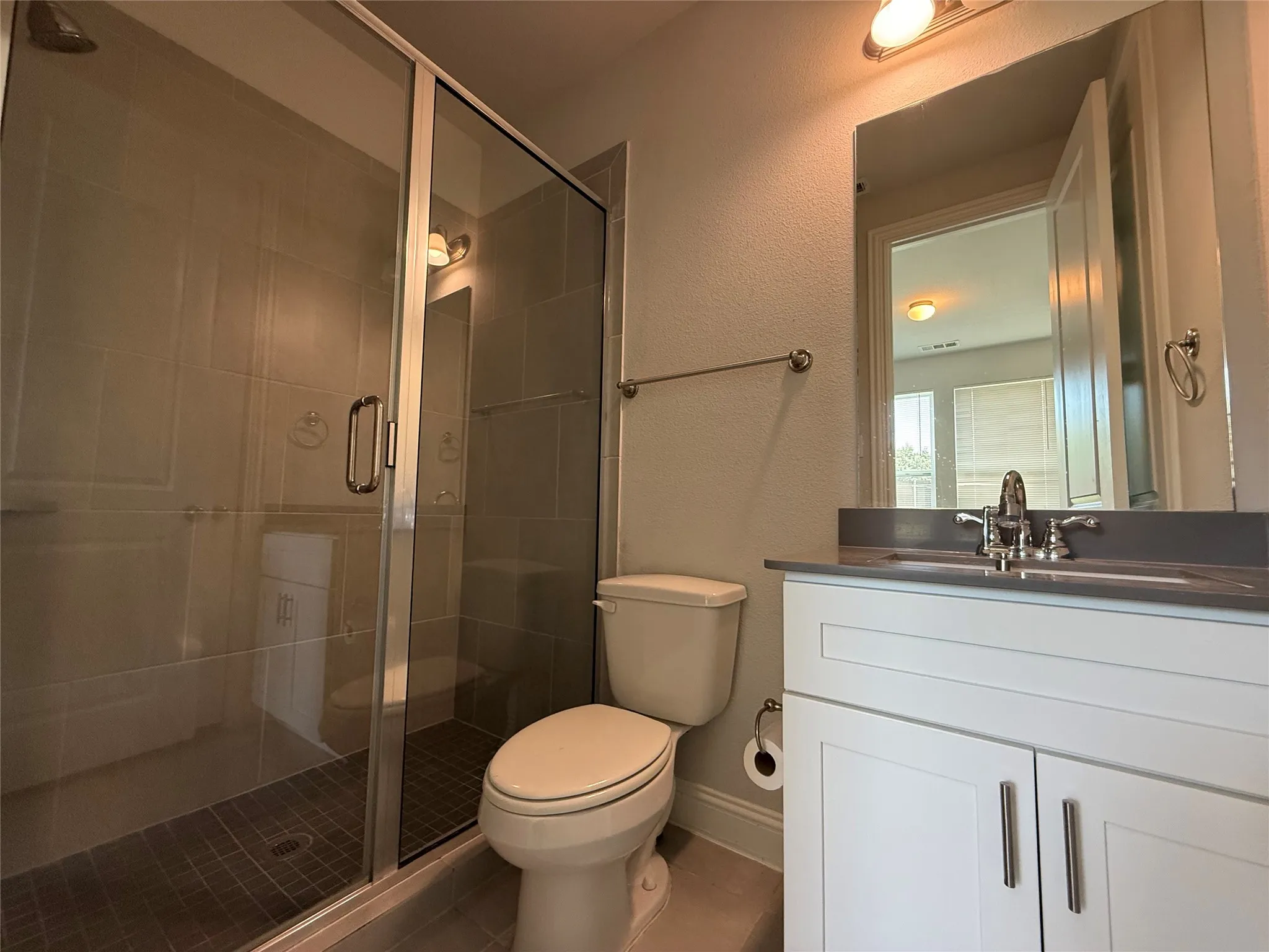 Glass-enclosed shower with tile surround, white vanity with integrated sink, chrome fixtures, and a wall-mounted mirror