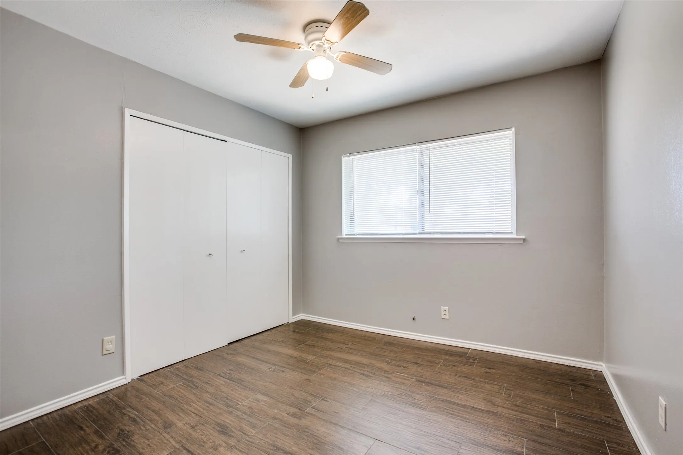 Wood-finish flooring, ceiling fan with integrated lighting, window with horizontal blinds, and closet with sliding panel doors