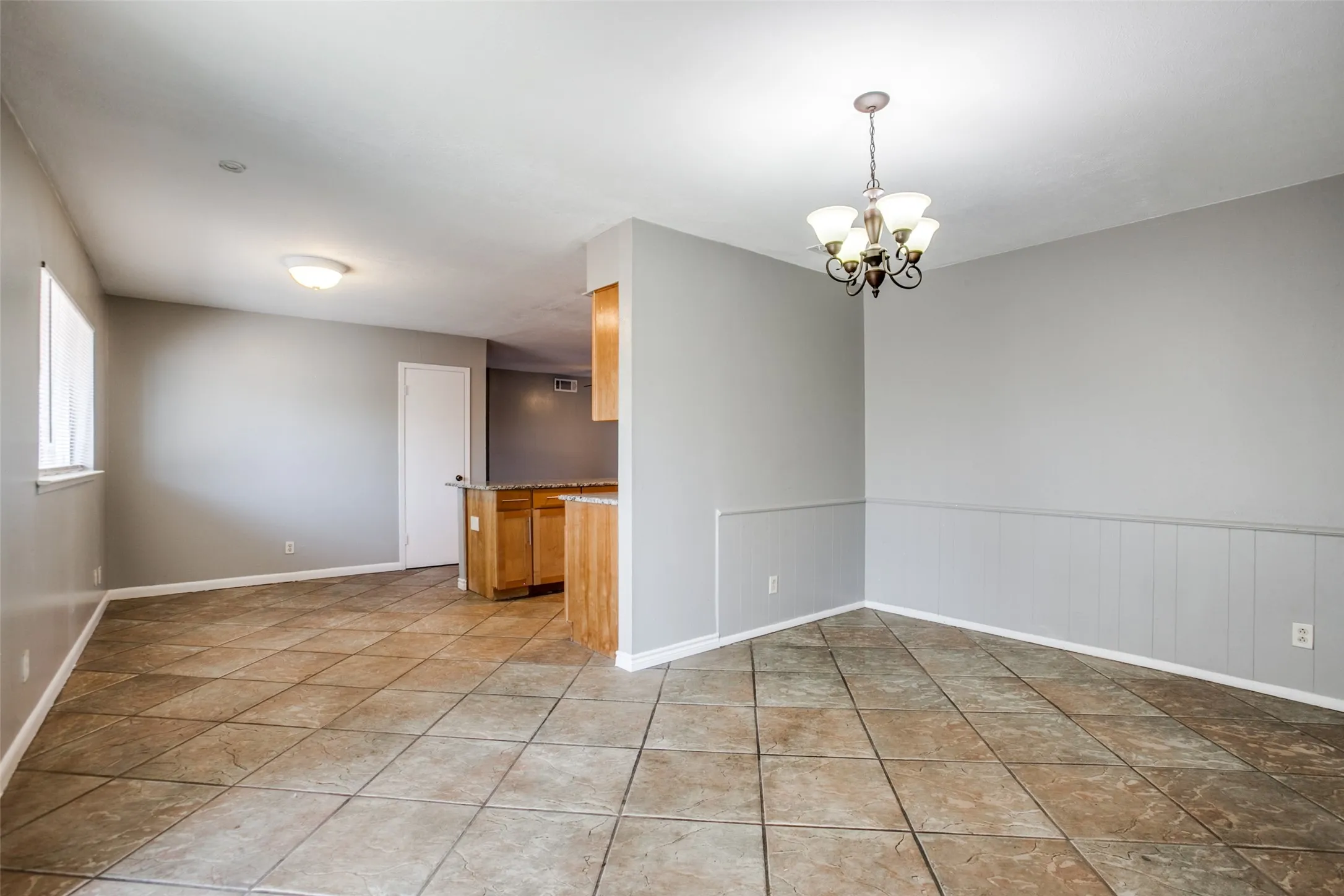 Spacious room featuring tile flooring, wainscoting, an overhead chandelier, and a breakfast bar with wood-finish cabinetry