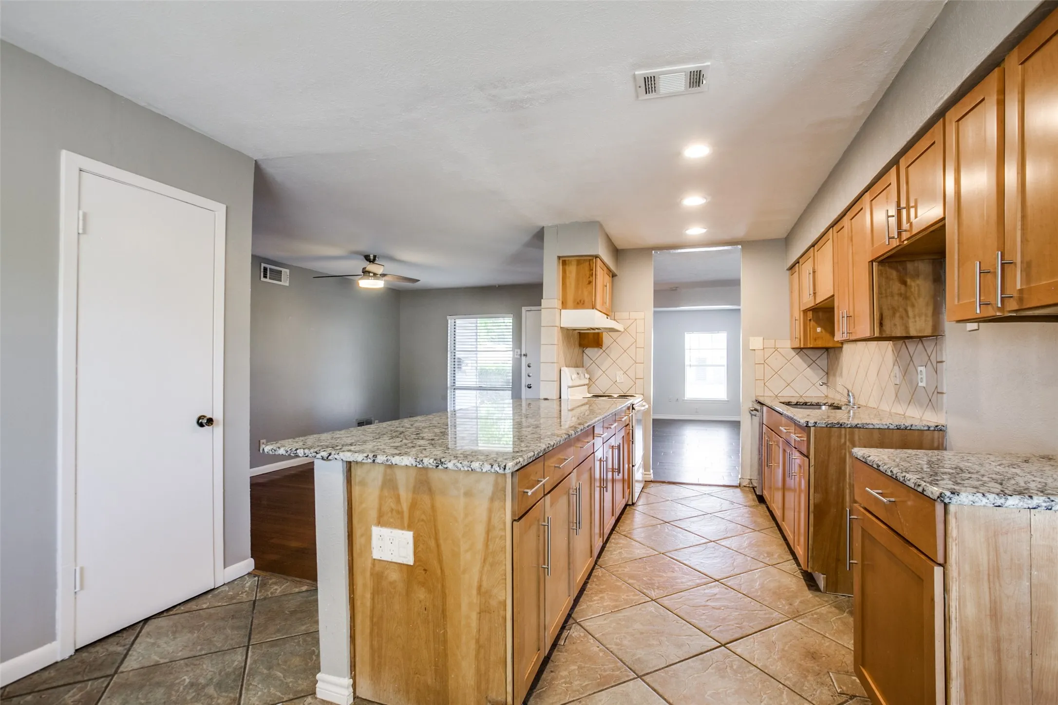 Galley kitchen featuring wood-finish cabinetry, granite countertops, stainless steel appliances, and ceramic tile flooring