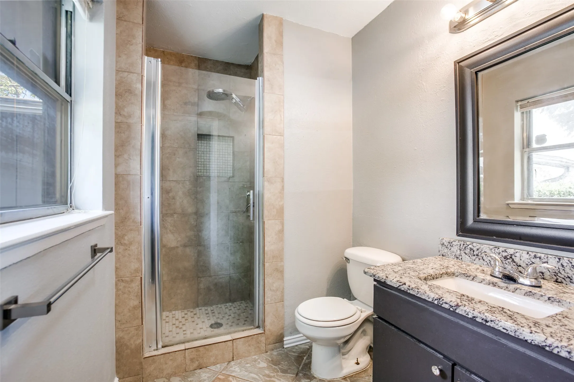 Glass-enclosed shower with tile surround, vanity with stone countertop, undermount sink, and dark wood cabinetry