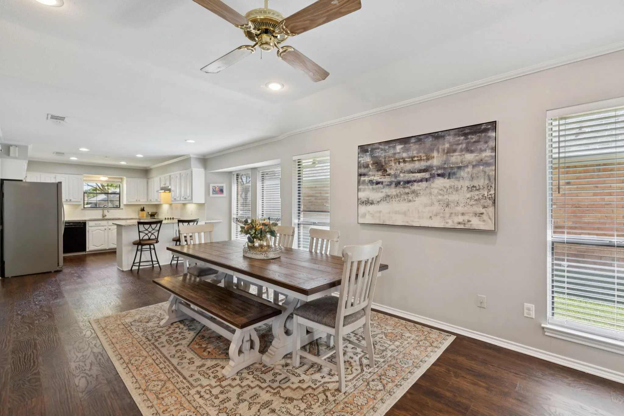 Wood-finish flooring throughout, tray ceiling with a ceiling fan, recessed lighting, and kitchen with white cabinetry and stainless steel appliances