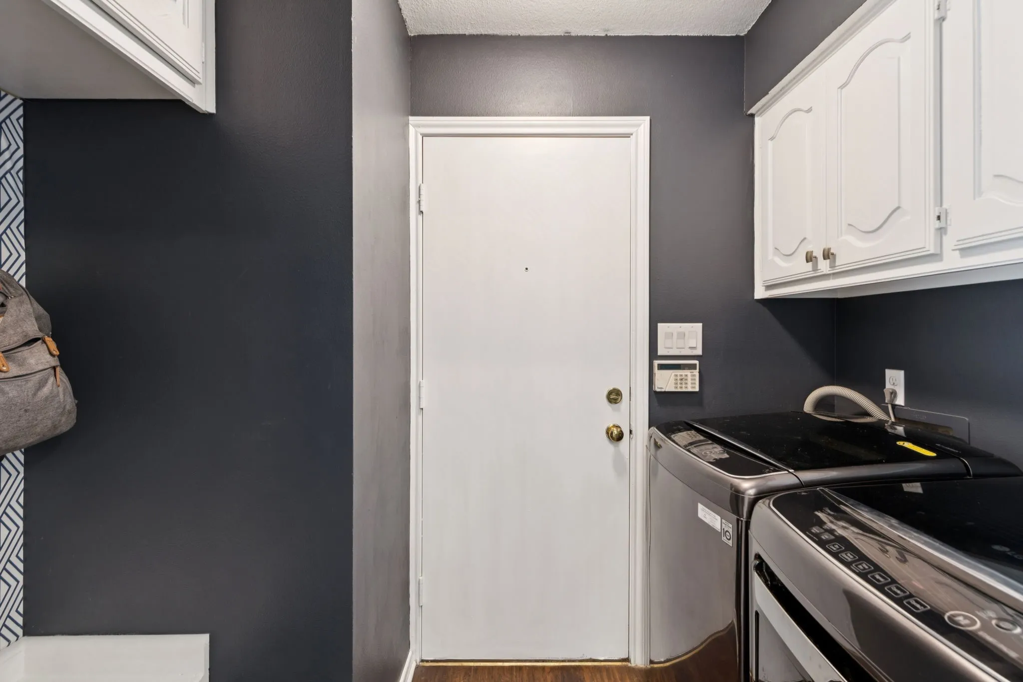 Integrated laundry area featuring white upper cabinetry, dark painted walls, and wood-finish flooring