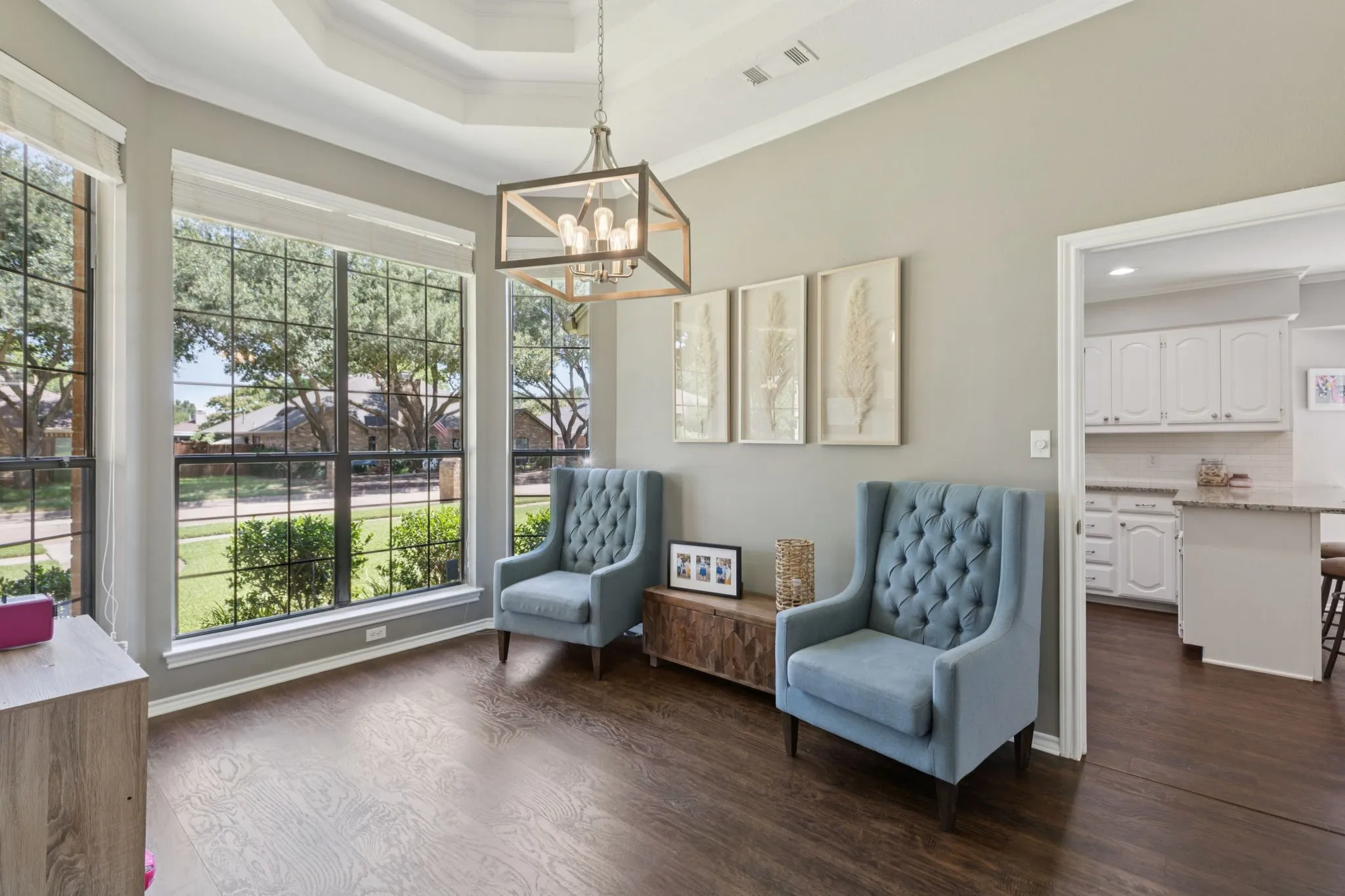 Tray ceiling with crown molding, wood-finish flooring, large multi-pane windows, and a decorative chandelier