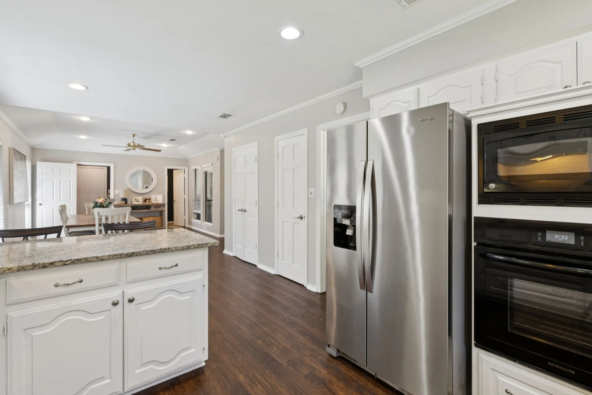 Kitchen featuring a granite-topped island with white cabinetry, stainless steel side-by-side refrigerator, built-in microwave, and wood-finish flooring