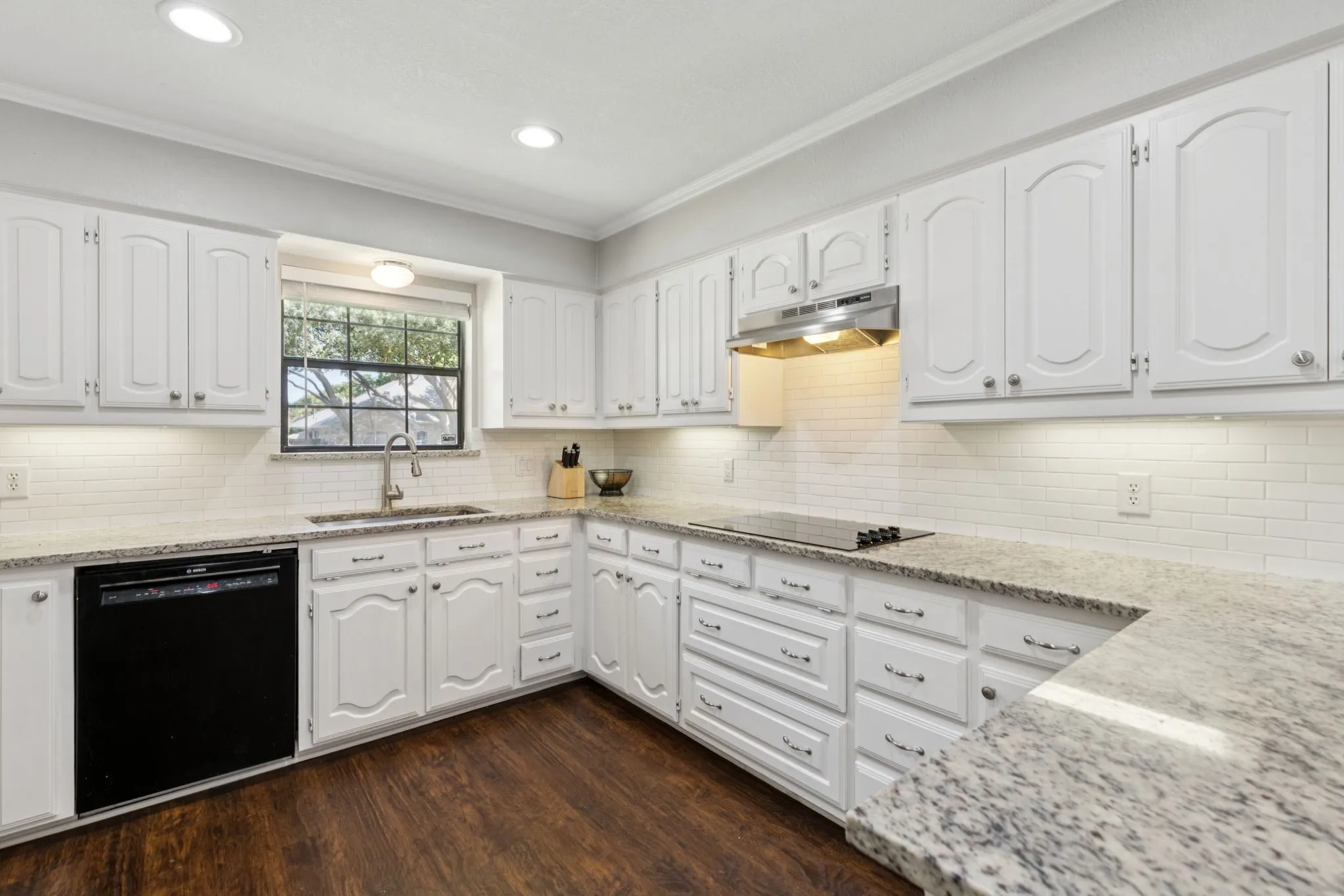 Kitchen featuring white cabinetry, granite-style countertops, wood-finish flooring, white subway tile backsplash, and a built-in cooktop