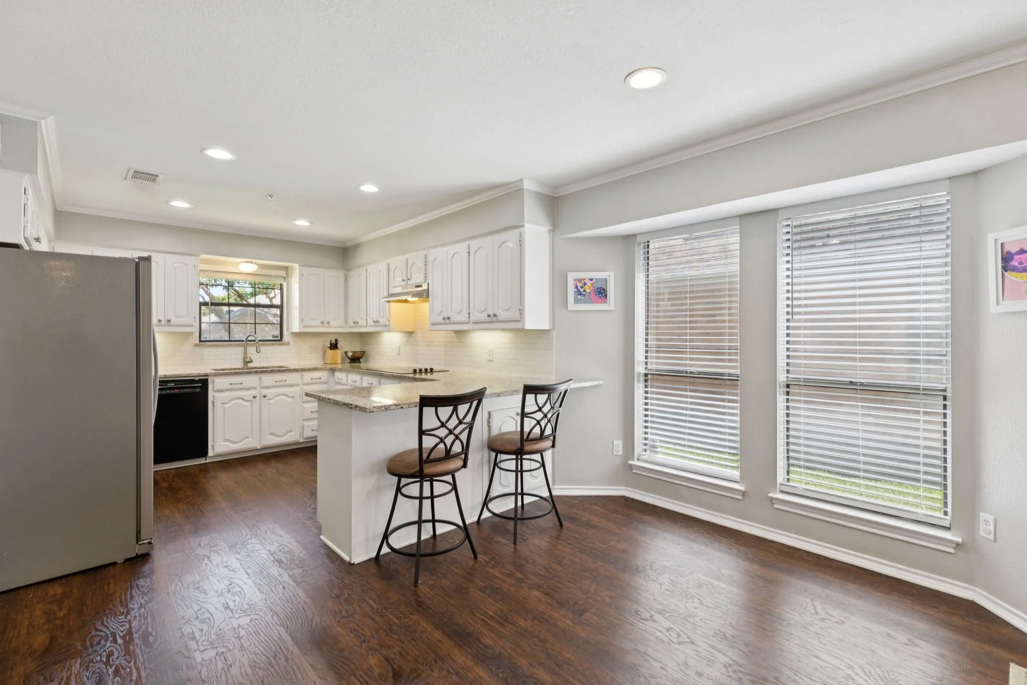 Kitchen featuring wood-finish flooring, white cabinetry, a kitchen island with seating, a stainless steel refrigerator, and recessed lighting