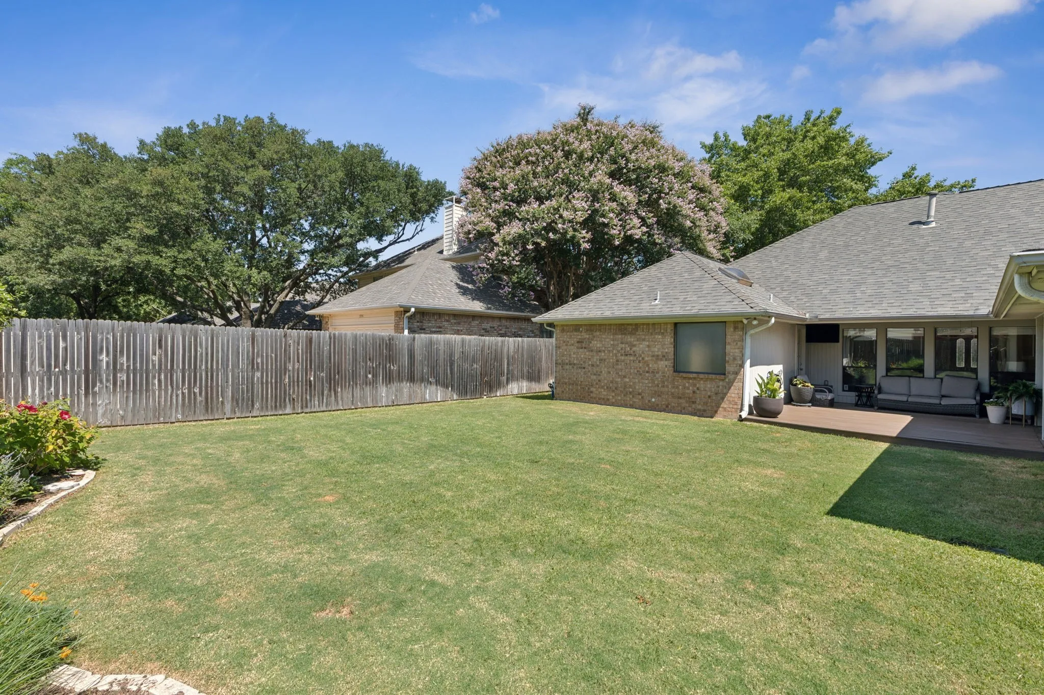 Expansive grassy yard with a privacy fence, mature trees, and a shaded outdoor patio
