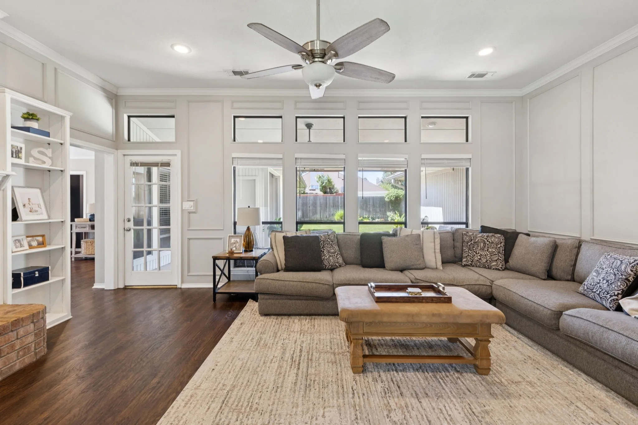 Expansive living area featuring wood-finish flooring, a ceiling fan, recessed lighting, built-in shelving, and multiple windows