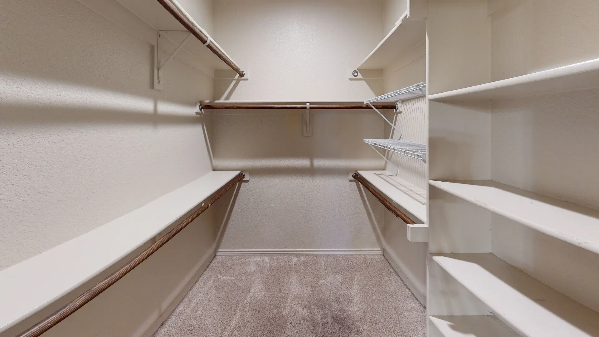 Carpeted flooring with built-in shelving, hanging rods, and wire shelving