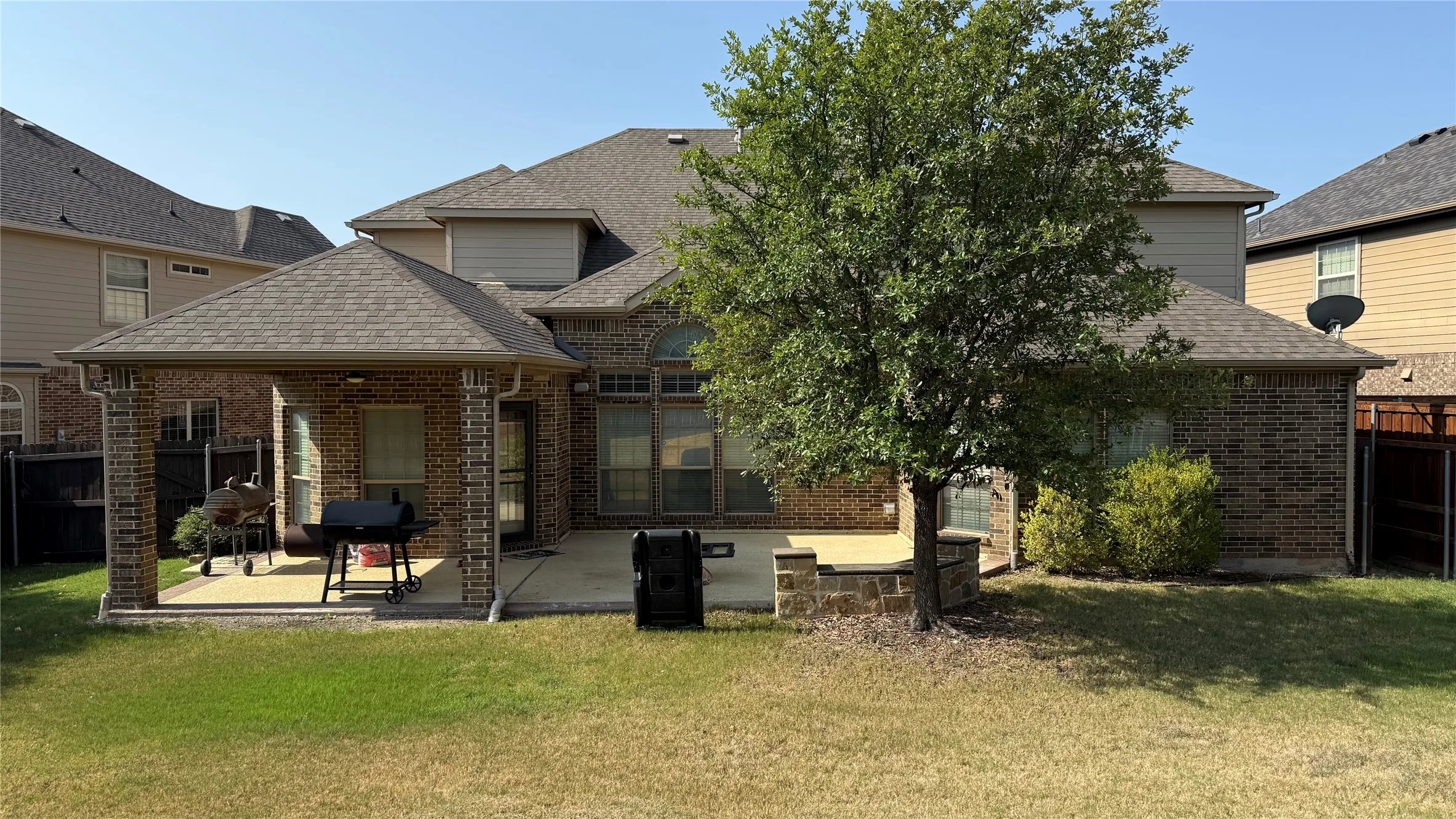 Covered patio with brick columns, concrete patio area, and mature landscaping