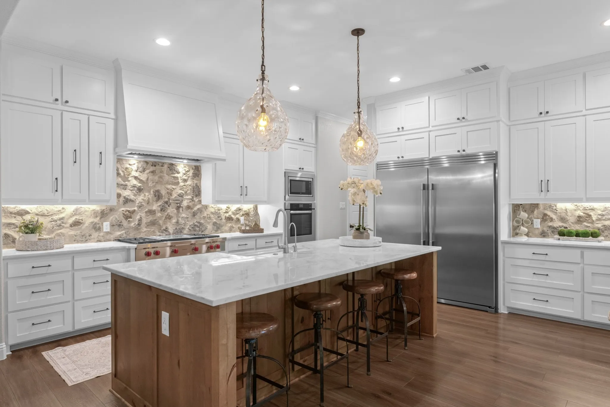 The spectacular kitchen features floor-to-ceiling cabinetry, an oversized island, butlers & walk in pantry, special-order quartz countertops, real-cut stone backsplash, farmhouse sink, commercial-style faucet, pot filler, double convection ovens & premium appliances.