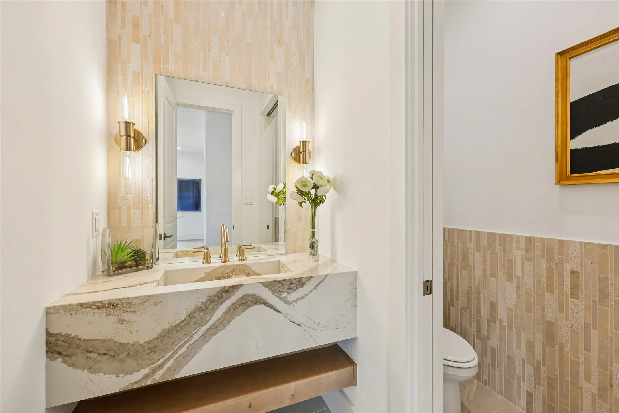Floating vanity with integrated basin, gold-finish fixtures, and a large mirror