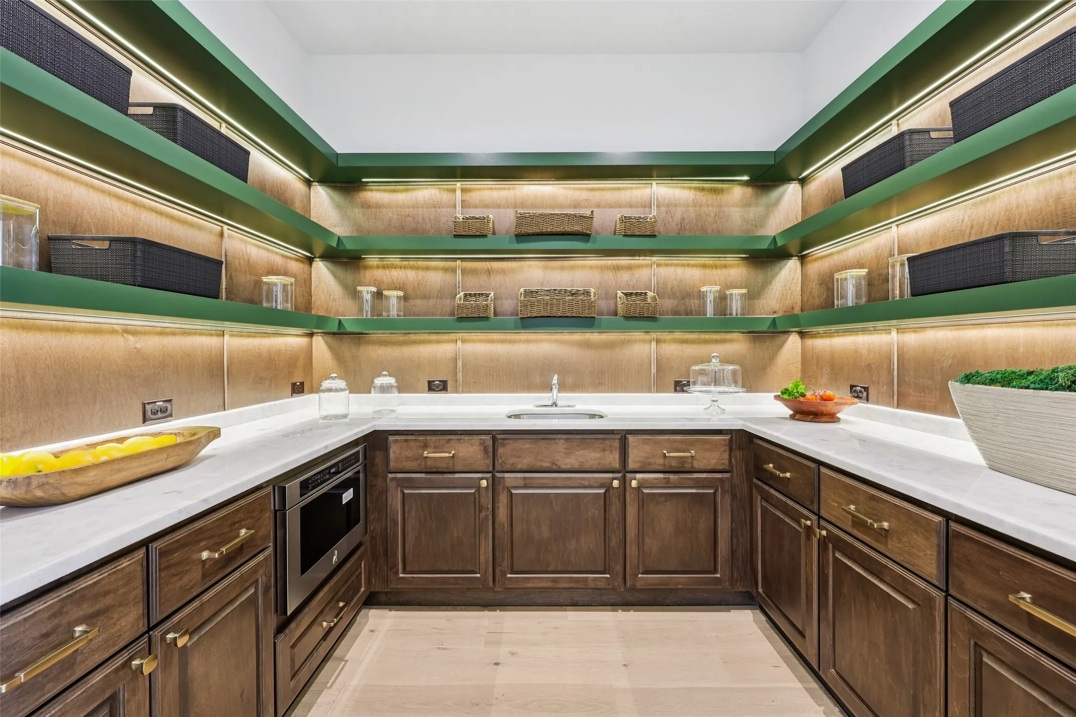 U-shaped countertop with integrated sink, rich wood cabinetry with gold-tone hardware, built-in microwave, and open shelving with integrated lighting