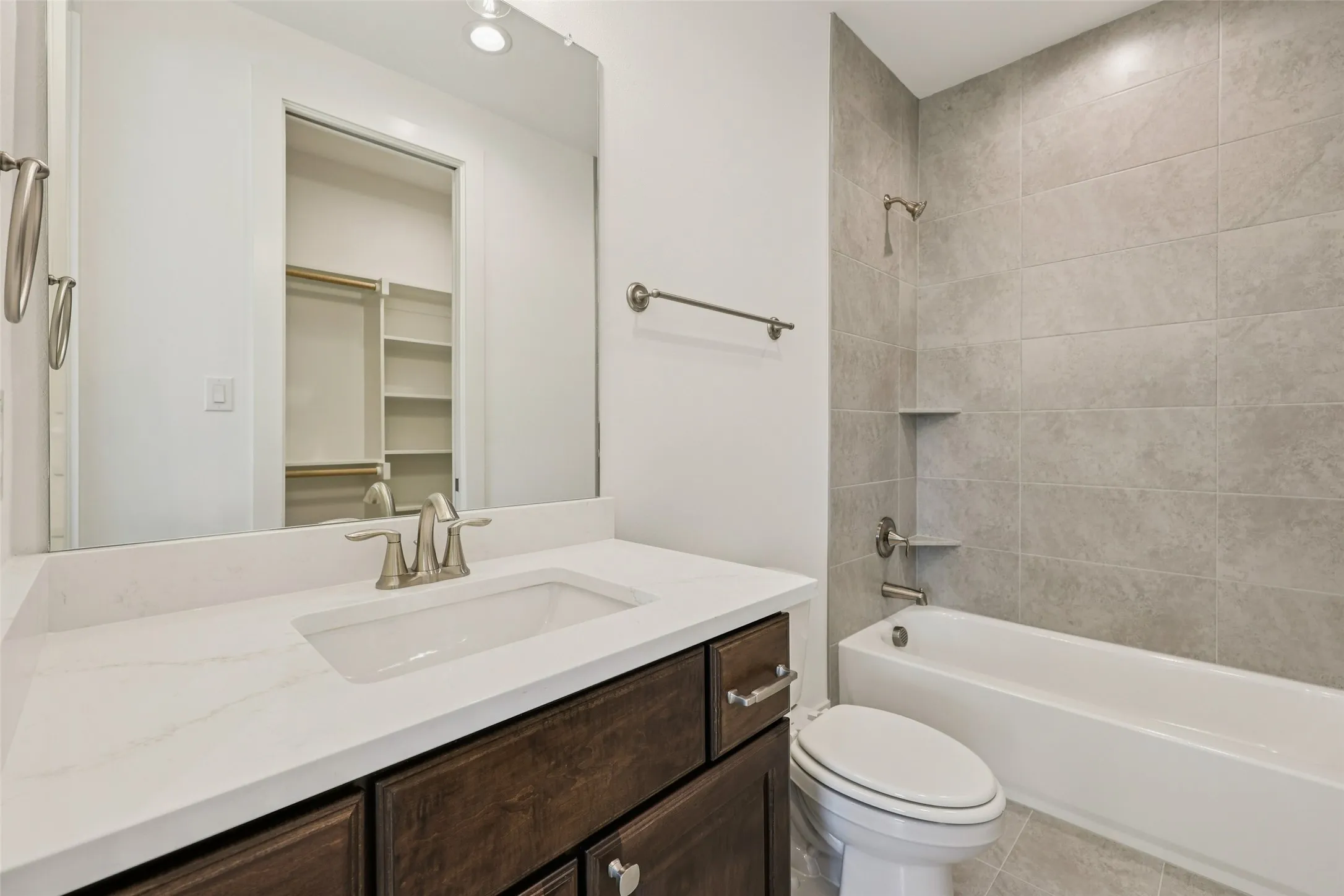 Bathroom featuring a vanity with a white countertop and undermount sink, dark wood-finish cabinetry, a bathtub with a tiled surround, and integrated shelving