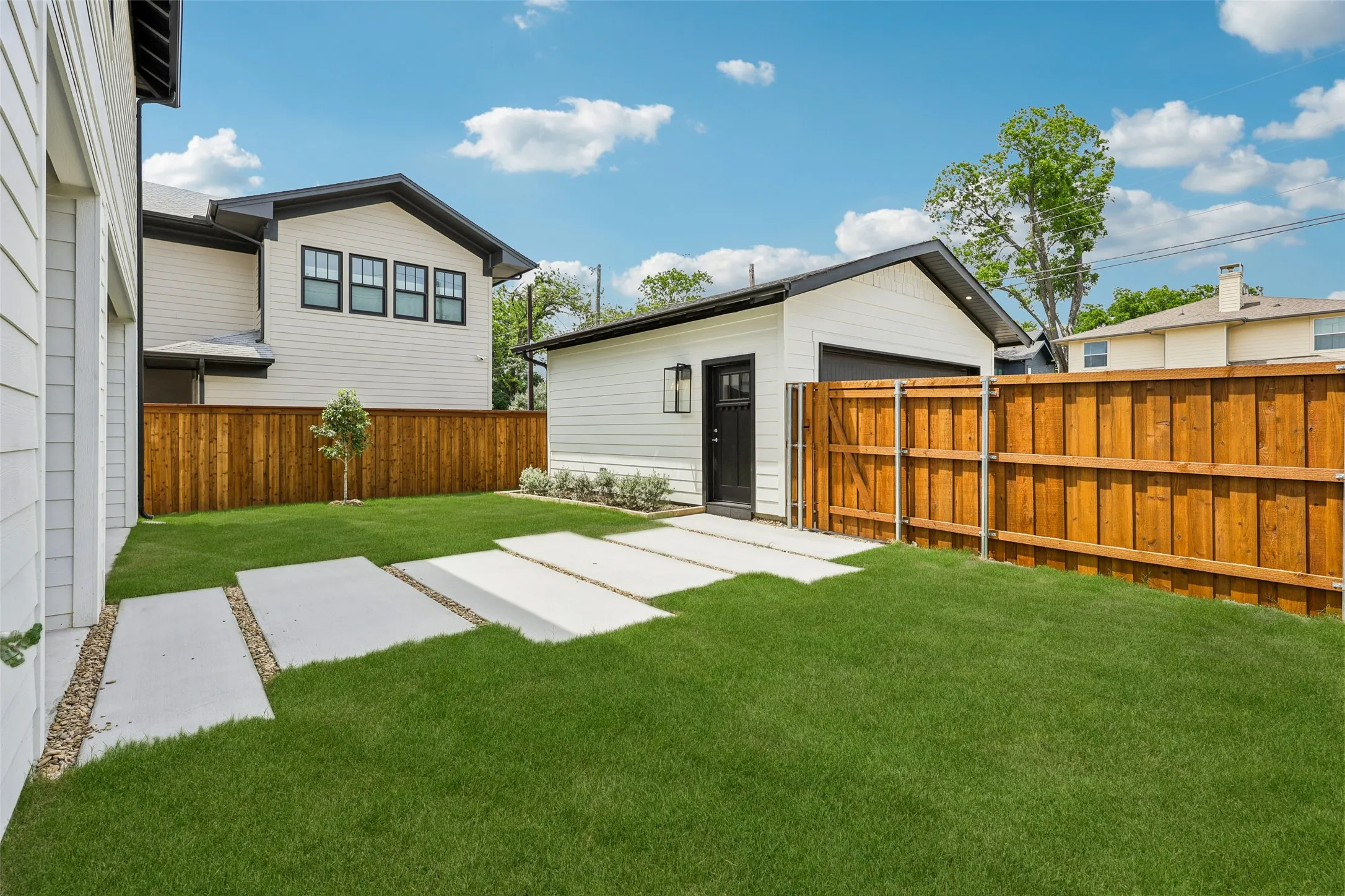 Expansive lawn with concrete stepping stones, wood fencing, and a detached garage with a dark-framed entry door